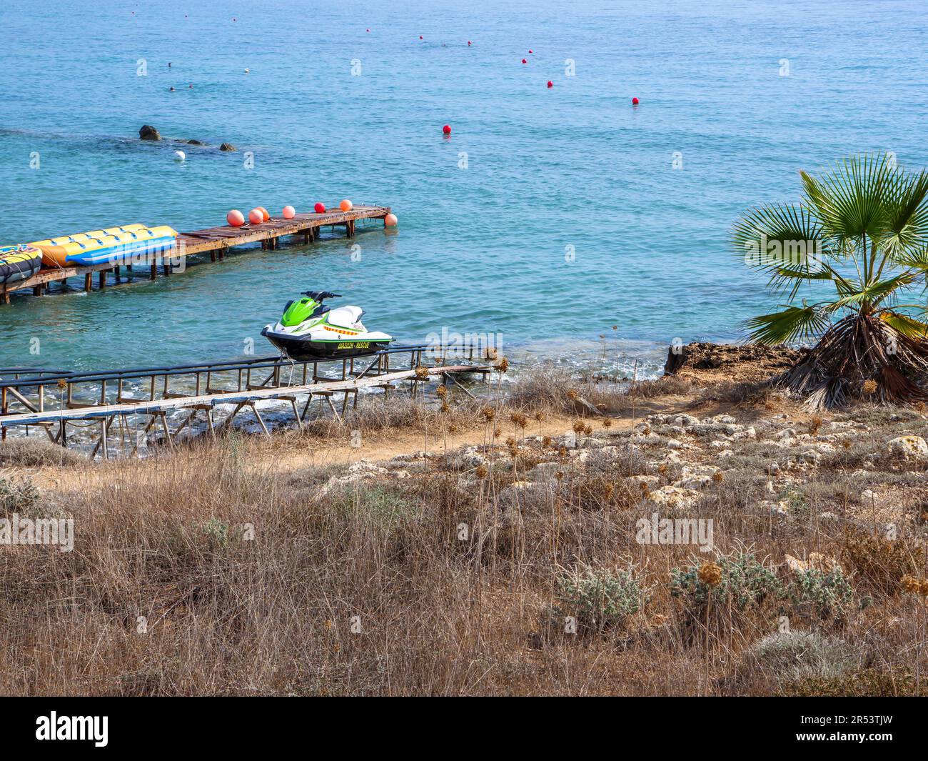 Sauvetage de scooter d'eau sur des rails à la rive, bananiers gonflables, et bouées rouges sur le ponton en arrière-plan et dans la mer Méditerranée. Banque D'Images