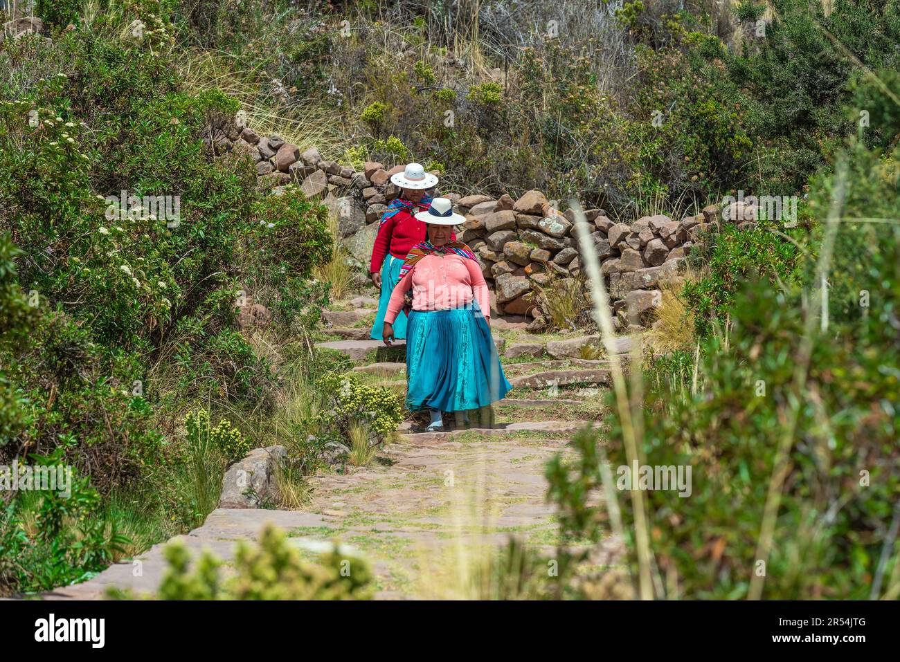 Deux femmes quechua indigènes en vêtements traditionnels marchant sur le chemin du port d'Isla Taquile (île de Taquile), lac Titicaca, Pérou. Banque D'Images