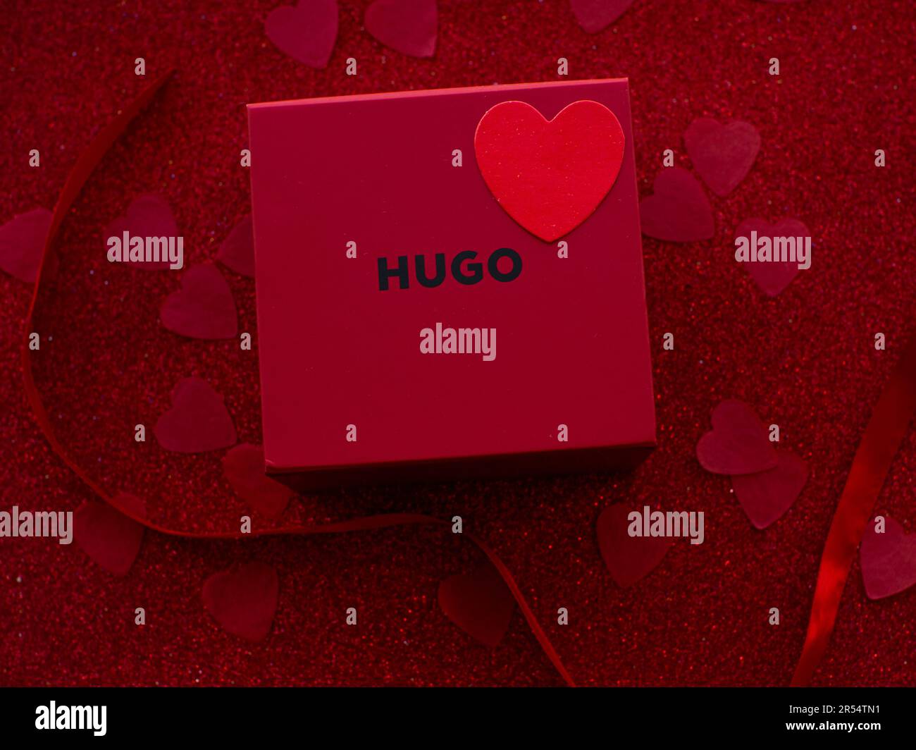 Hugo par Hugo Boss. La boîte cadeau rouge est sur fond de papier cœur  rouge, vue du dessus. Carte de vœux, présente. Concept de vacances de  Saint-Valentin. Poser à plat avec un