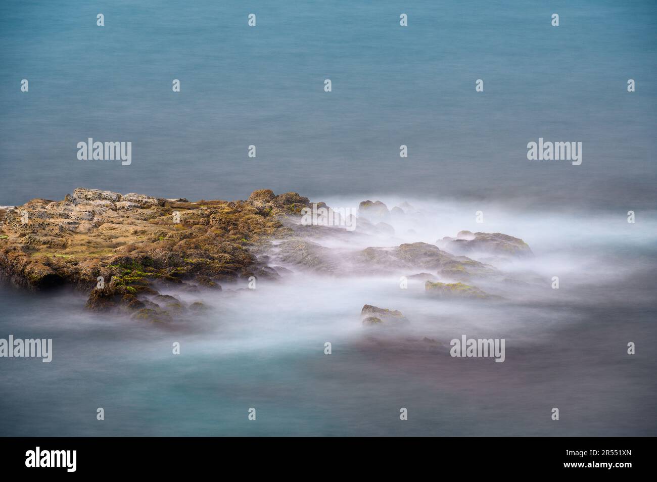 L'eau de mer bat sur les roches brunes, produisant un jet blanc. Vue sur l'île Keelung depuis la plage de Wanli à New Taipei. Taïwan. Banque D'Images