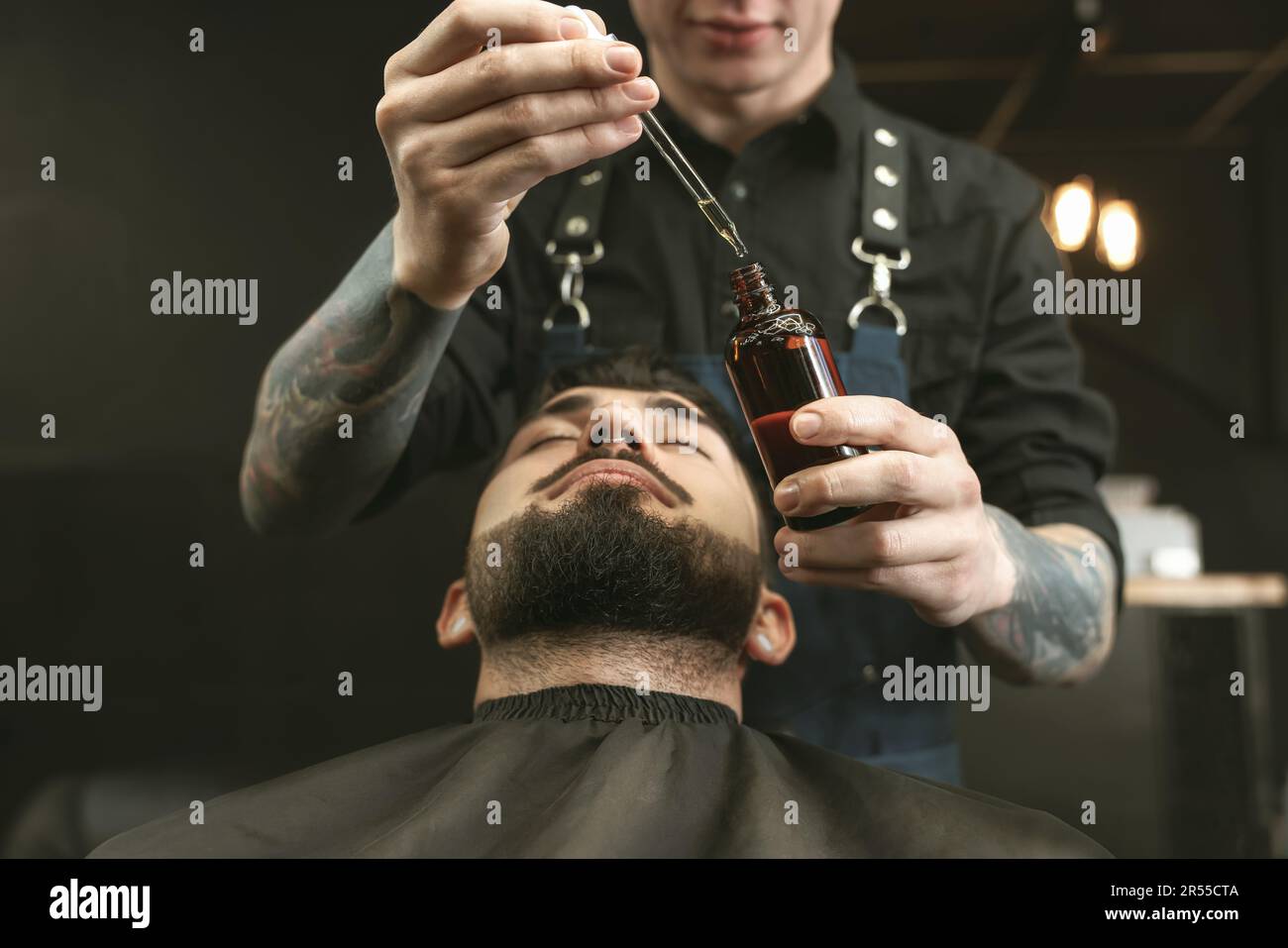 Coiffeur avec de l'huile de barbe près du client dans le salon de coiffure, en gros plan. Service de rasage professionnel Banque D'Images