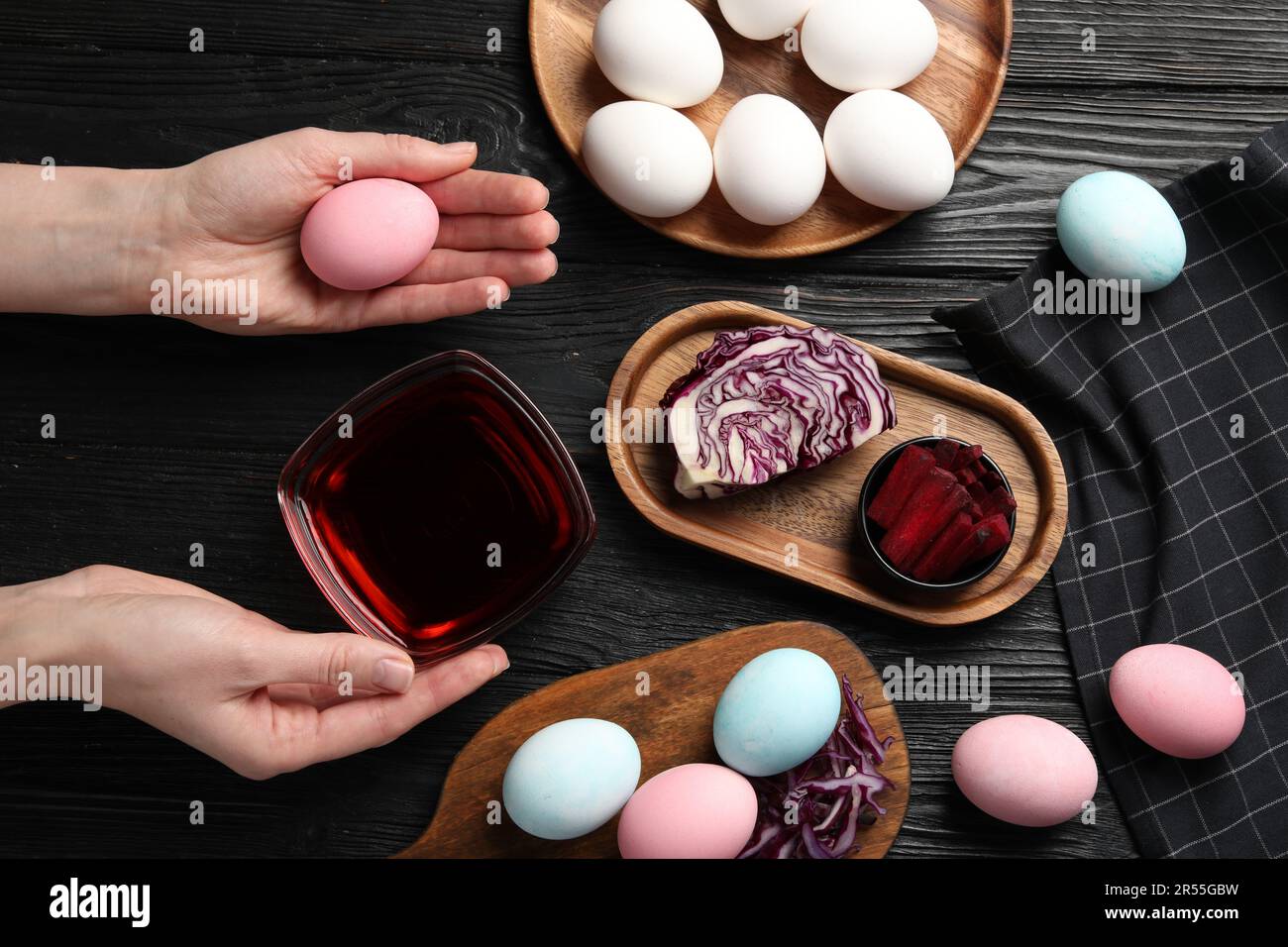 Femme tenant un œuf de Pâques peint avec des teintures naturelles sur une table en bois noir, vue de dessus. Betterave utilisée pour la coloration Banque D'Images