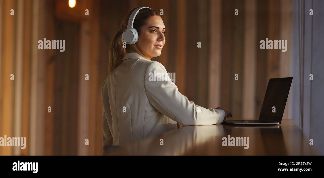 Femme professionnelle portant un casque sans fil dans un espace de coworking. femme d'affaires écoutant de la musique tout en travaillant sur un ordinateur portable. Femme travaillant à distance Banque D'Images