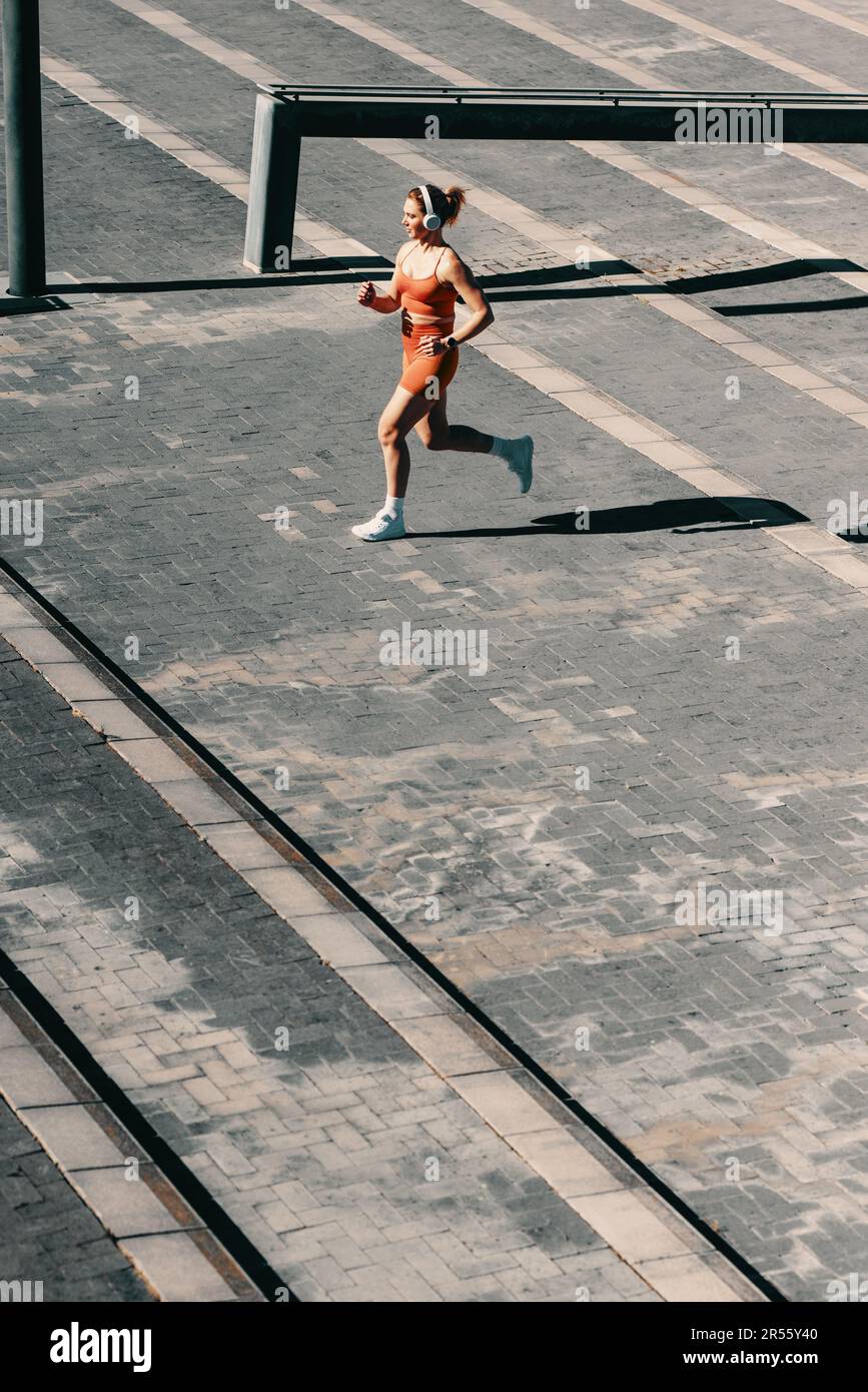 Femme sportive dans ses 30s rester active et en forme en faisant de l'exercice à l'extérieur. Elle porte des vêtements de sport colorés, avec son casque et ses écouteurs, Banque D'Images