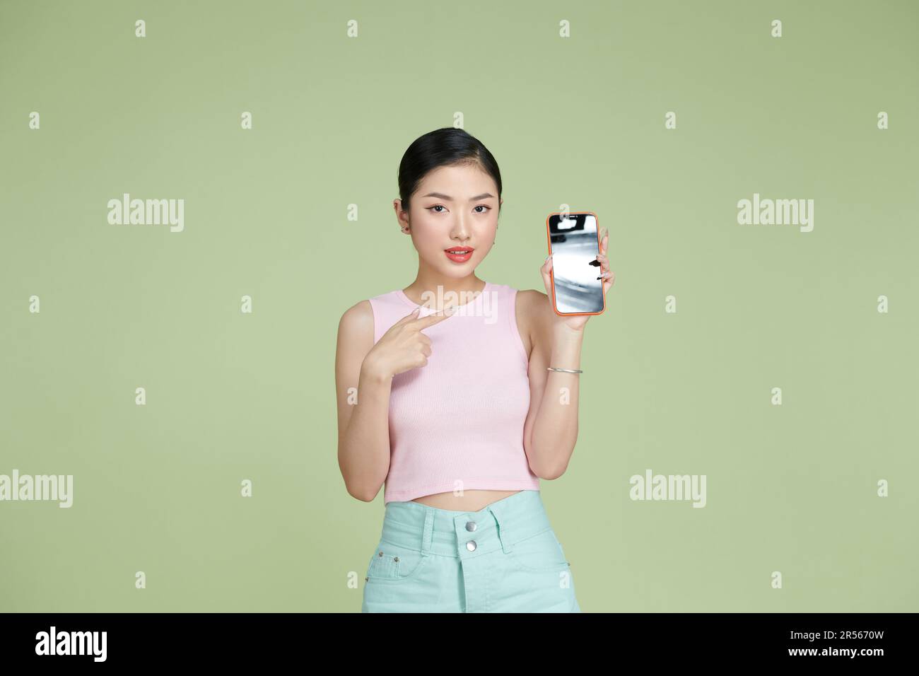 Une jeune femme asiatique tient le téléphone à la main et le pointe avec une expression ludique Banque D'Images