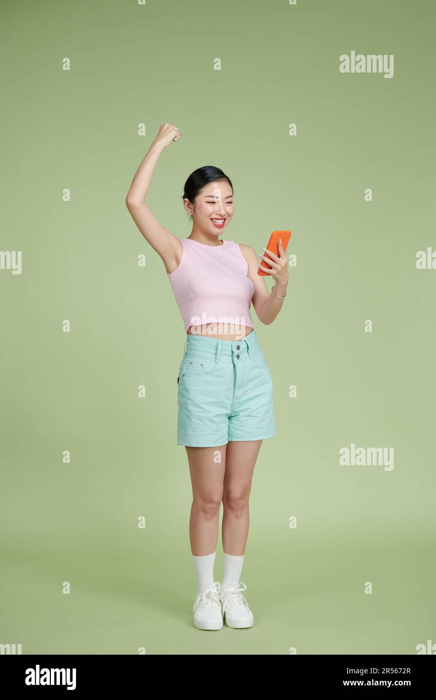 Portrait d'une jeune femme heureuse célébrant avec un téléphone portable isolé sur fond vert. Banque D'Images