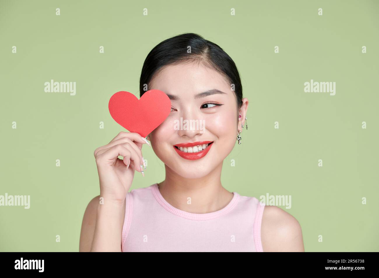 Jolie femme asiatique avec un sourire éclatant tout en tenant la carte de la Saint-Valentin entre les mains, Banque D'Images