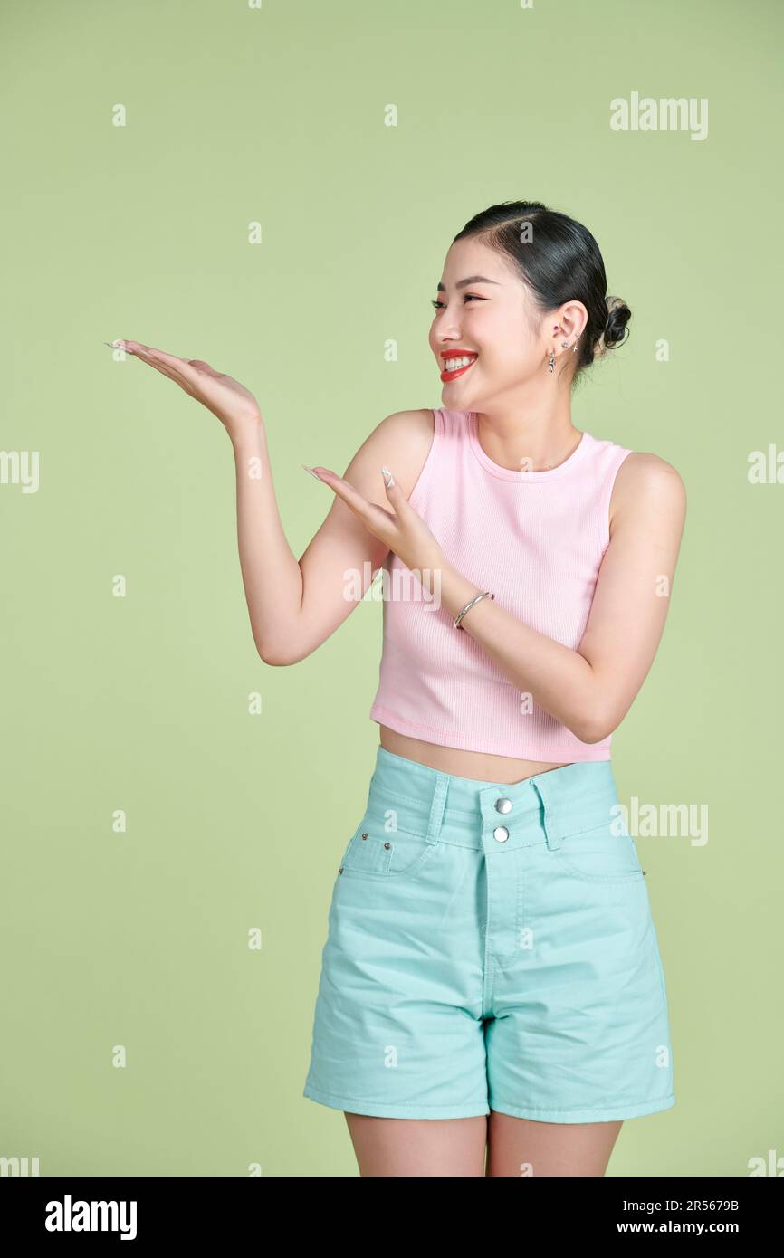 Femme asiatique mignon sourire debout présentant le produit tenant quelque chose sur le côté paume sur fond vert Banque D'Images