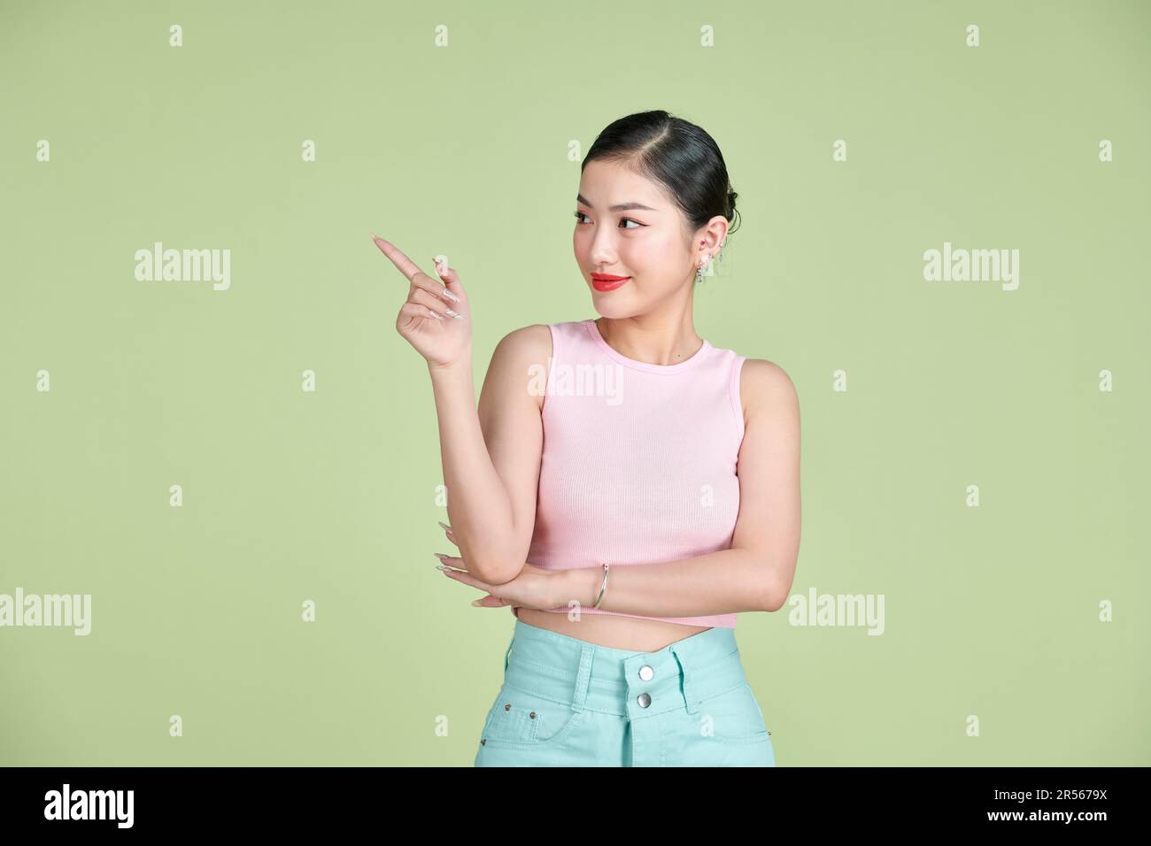 Jeune élégante belle femme asiatique souriant et pointant vers un espace de copie vide isolé sur fond vert Banque D'Images