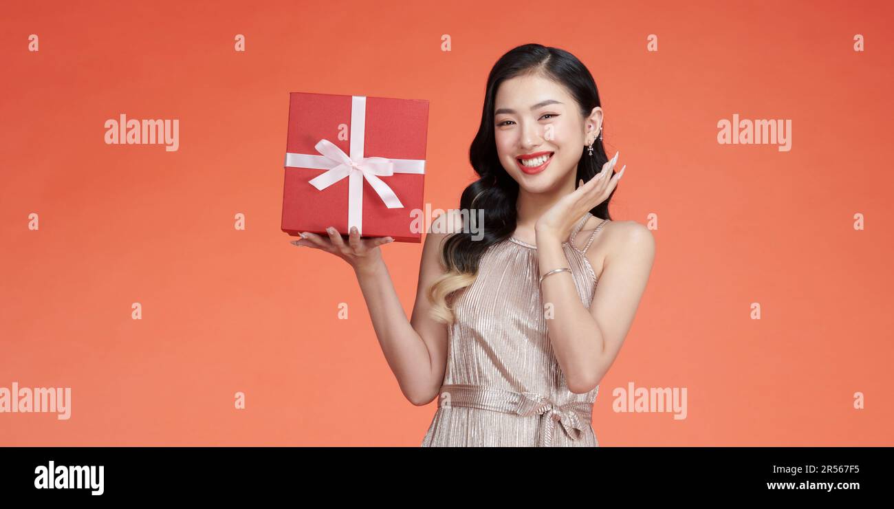 Jeune femme pensive en soirée tenue présente boîte avec cadeau ruban noeud isolé sur fond rouge Banque D'Images