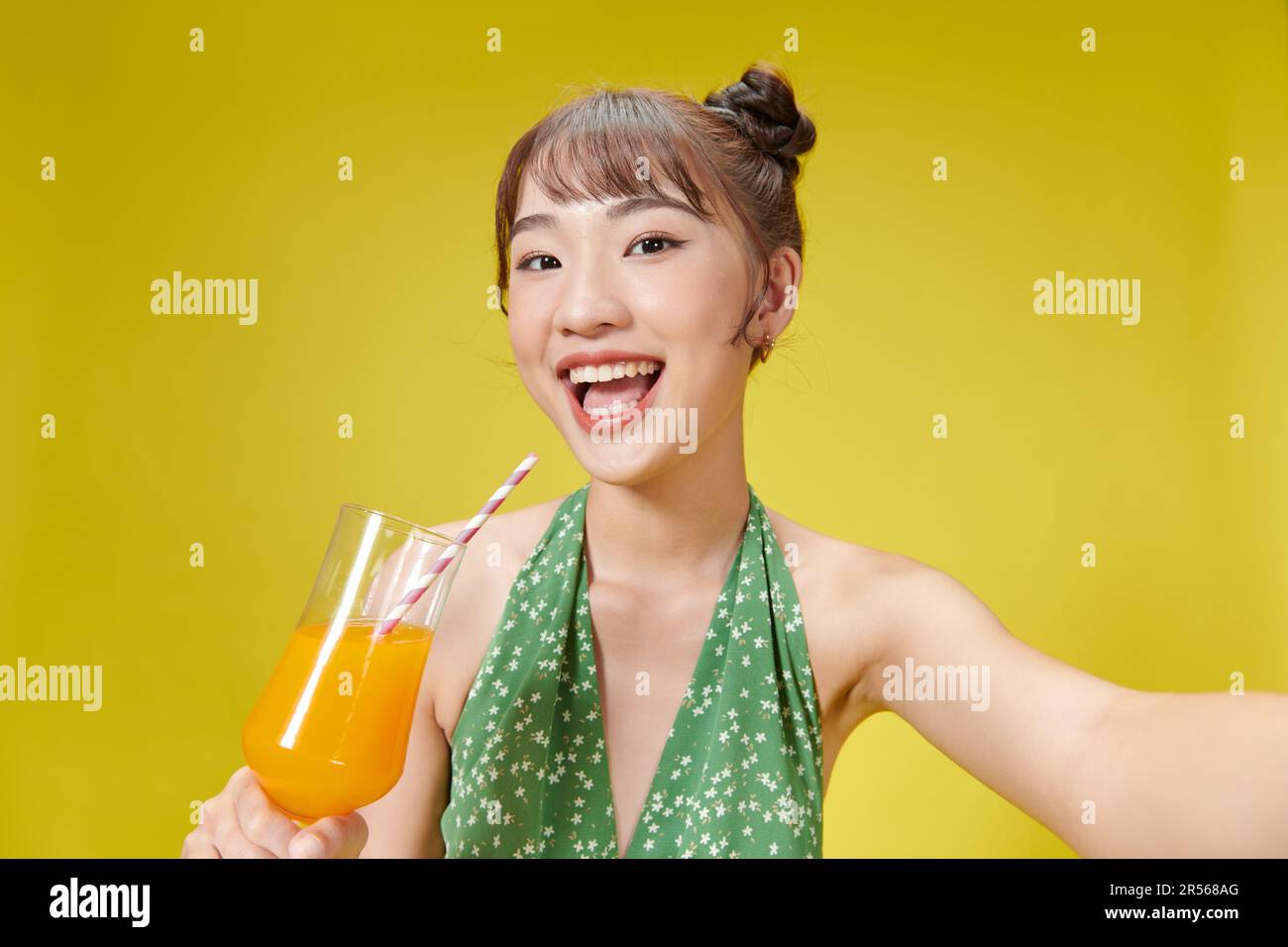 Charmante femme asiatique buvant du jus d'orange avec une paille tout en se tenant contre le jaune Banque D'Images