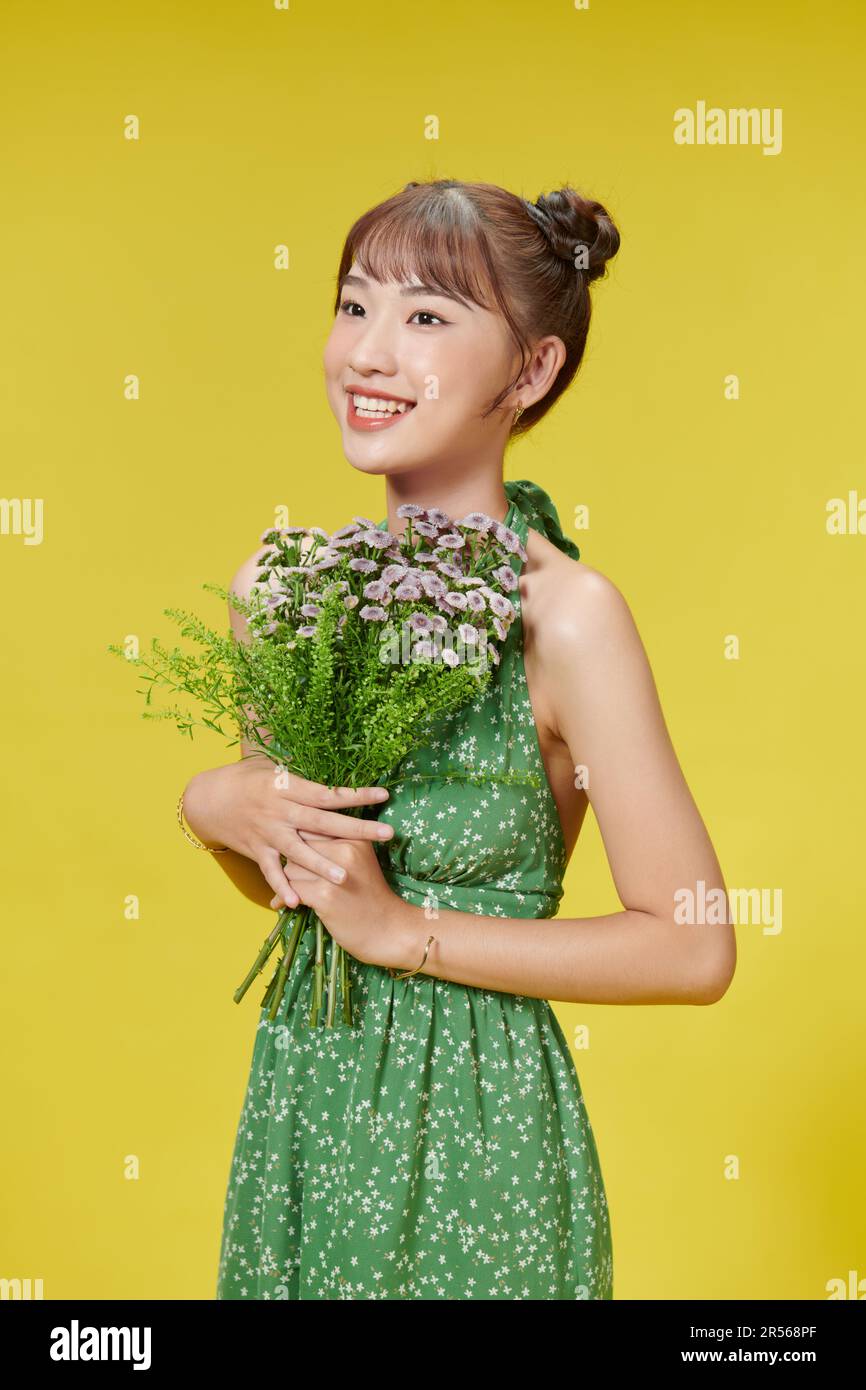 Portrait de jeunes sincères souriants isolés sur fond jaune clair, tenant des fleurs d'été colorées entre les mains, Banque D'Images