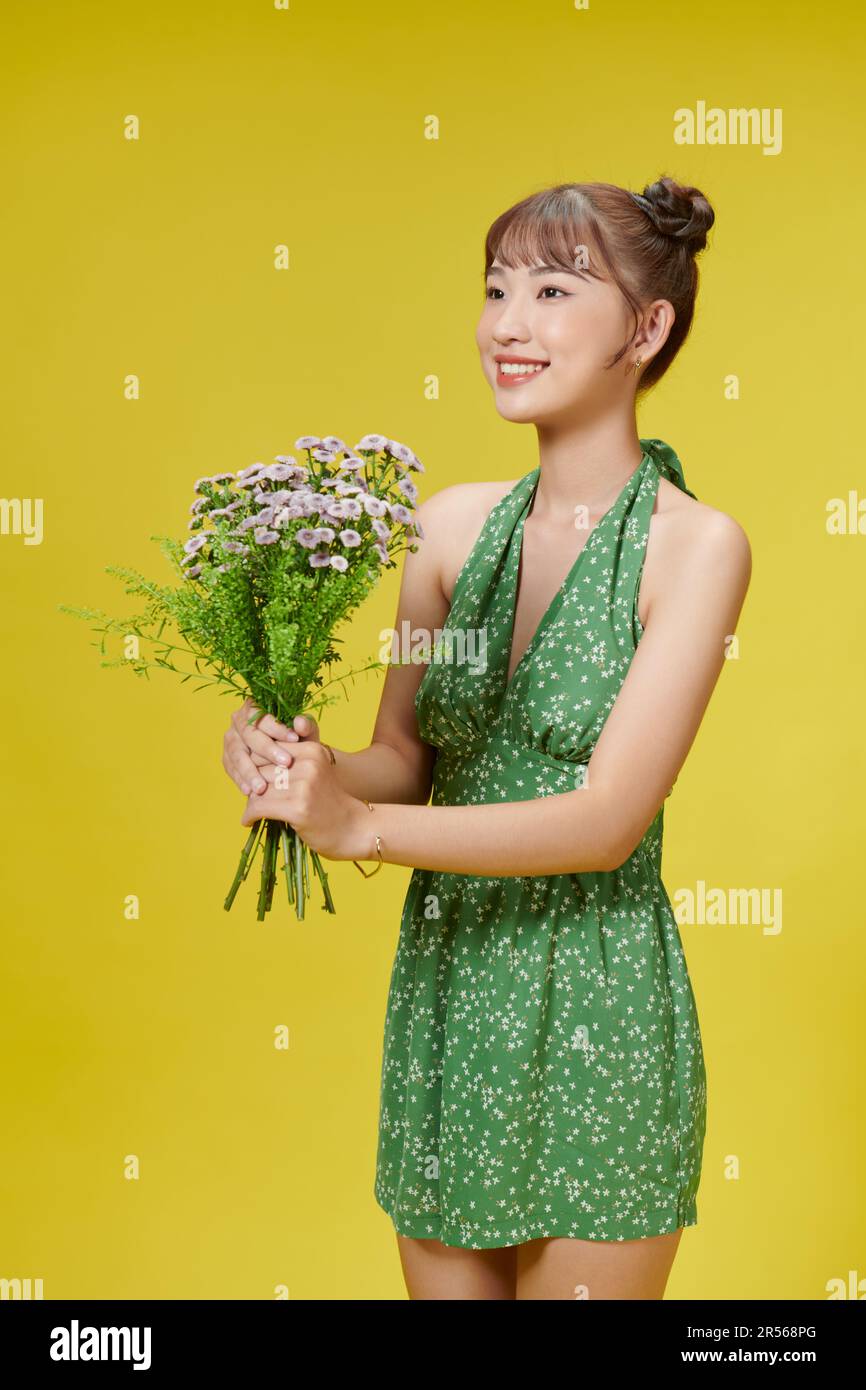 Une fille asiatique se tient sur un fond jaune embrassant un bouquet et souriant à l'appareil photo Banque D'Images