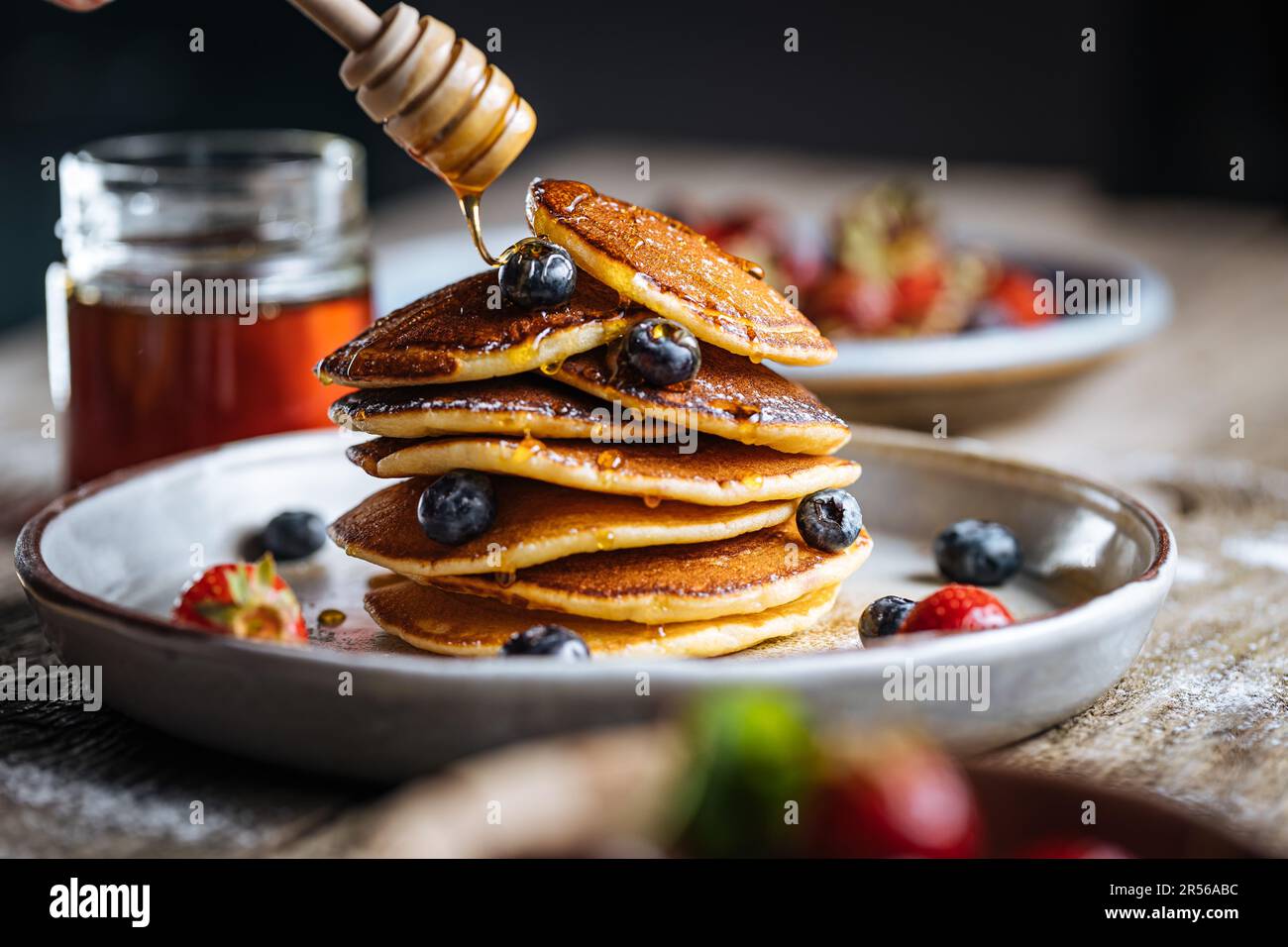 Crêpes américaines aux myrtilles, fraises et cerises avec trempette de miel. Placé sur une assiette de designer rustique, sur une planche rustique en bois. Banque D'Images