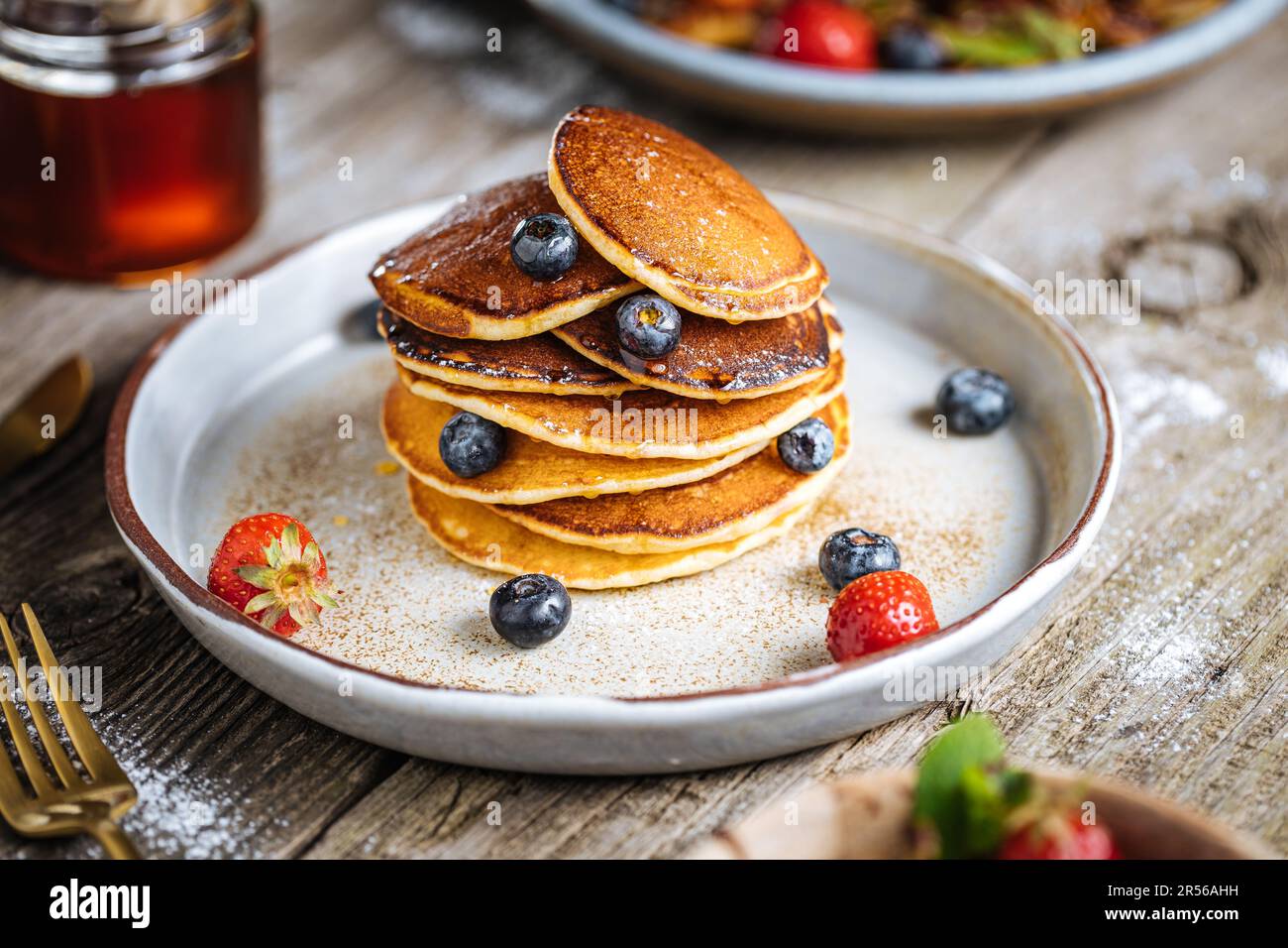 Crêpes américaines aux myrtilles, fraises et cerises avec trempette de miel. Placé sur une assiette de designer rustique, sur une planche rustique en bois. Banque D'Images