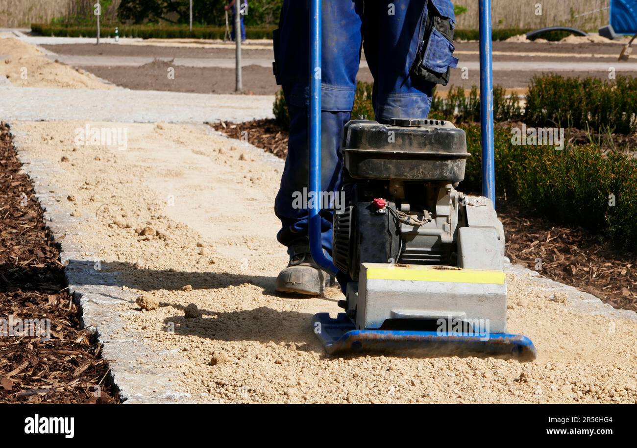 Jambes et pieds d'un homme qui utilise un compacteur de sable. L'homme vibre le sable d'un nouveau chemin. Banque D'Images