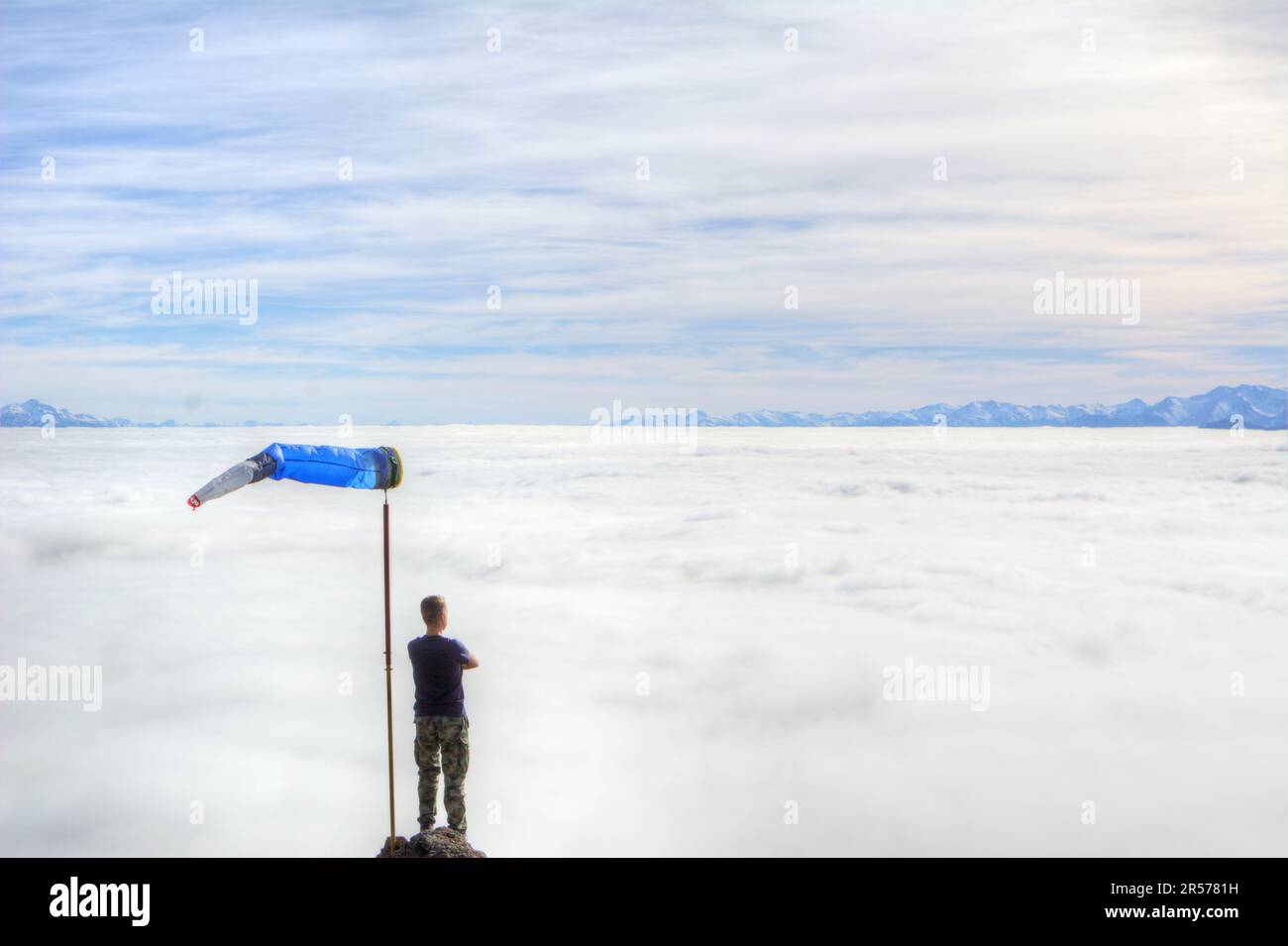 Un homme avec une grande girouette d'hiver regarde d'en haut les nuages sans neige couvrant une vallée de montagne à Bariloche, en Argentine Banque D'Images