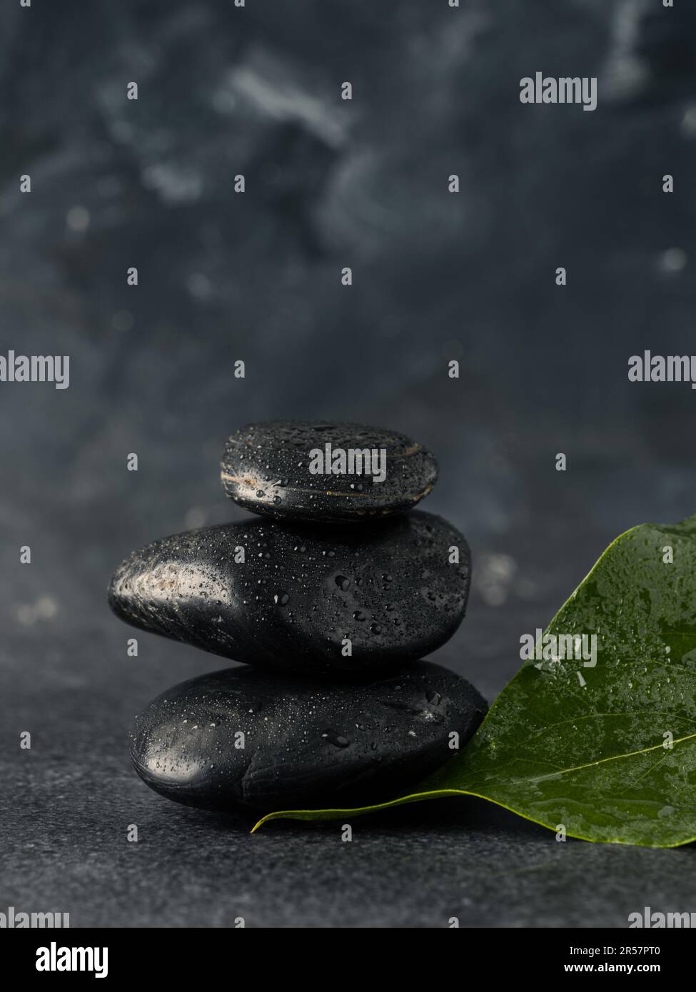 Pierres de massage empilées avec feuilles sur une table en pierre sombre, fond de spa Banque D'Images