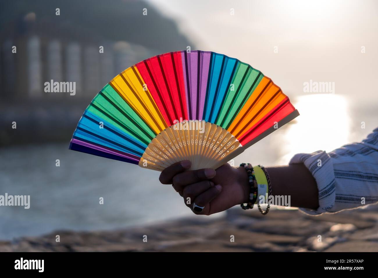 Fierté de la communauté LGBTQ. Main avec faux ongles dans les couleurs de l'arc-en-ciel tient le ventilateur arc-en-ciel Banque D'Images