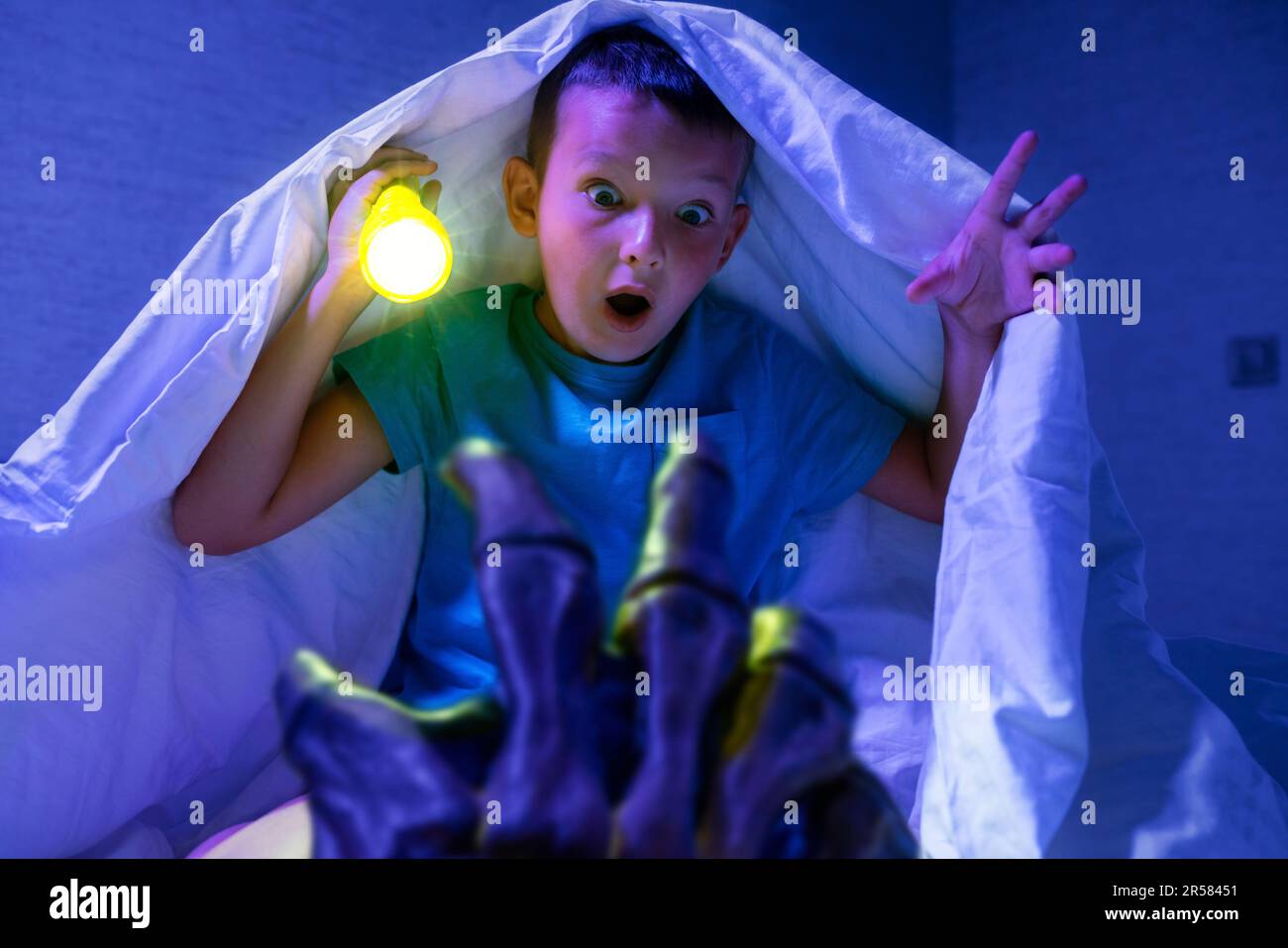 Un garçon effrayé avec une lampe de poche se cache sous une couverture de la main d'un monstre effrayant Banque D'Images
