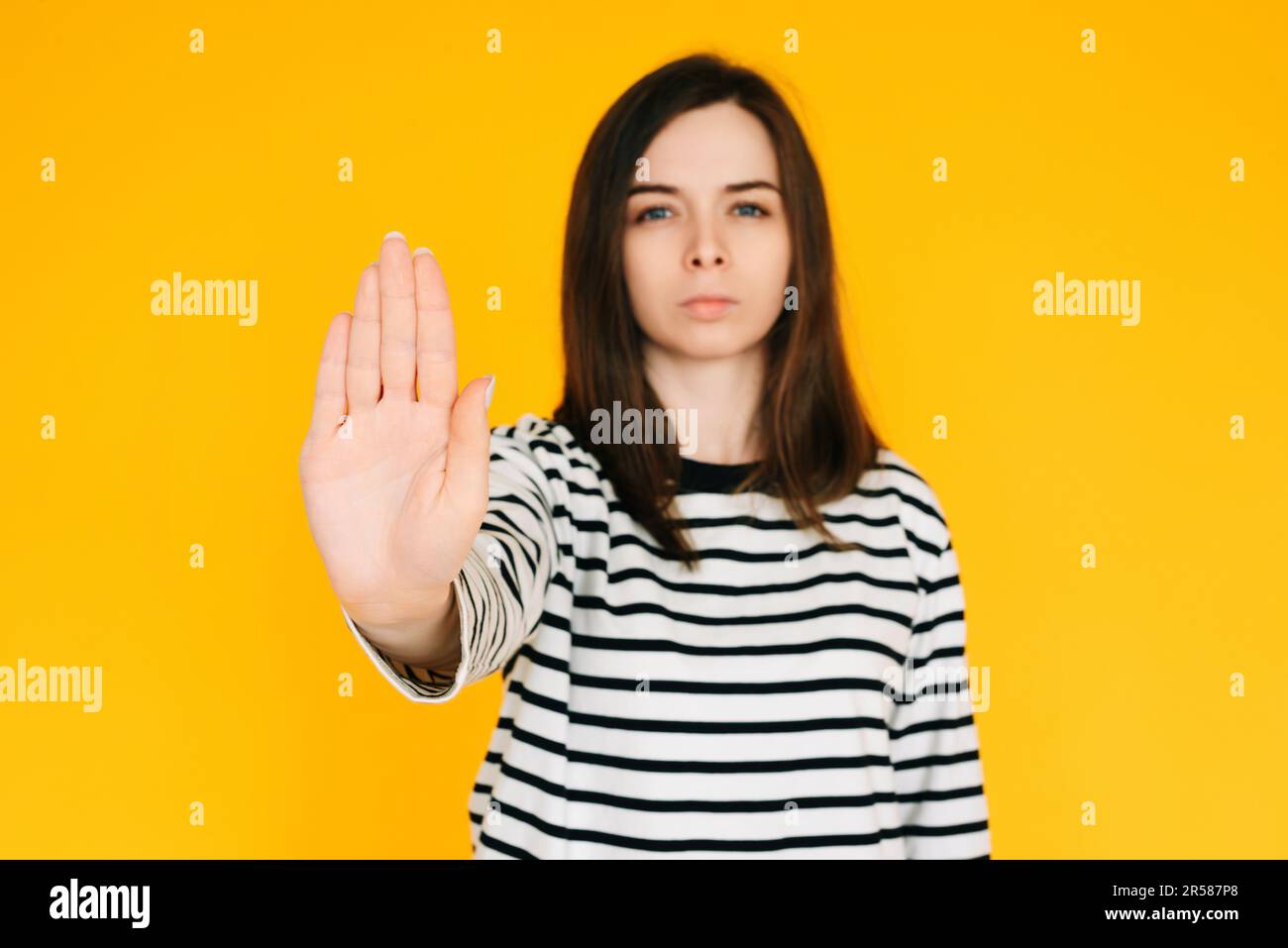 Femme déterminée faisant le stand: Femme sérieuse avec l'expression confiante levant la main dans le geste 'STOP' - concept d'assurance isolé sur vibrant Yello Banque D'Images