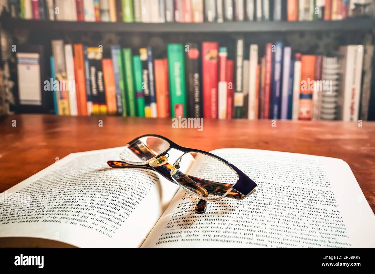 Ouvrez un livre et des lunettes avec des livres sur une étagère à l'arrière-plan. Faible profondeur de champ. Banque D'Images