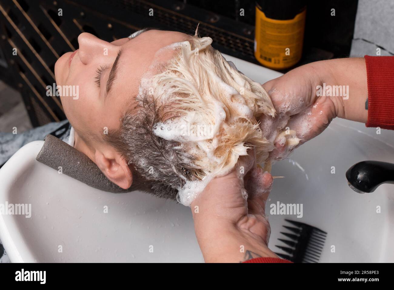 Un coiffeur lave ses cheveux et ses cheveux avec de la mousse dans le lavabo d'un client de coiffeur avant de couper et de teindre ses cheveux. Banque D'Images