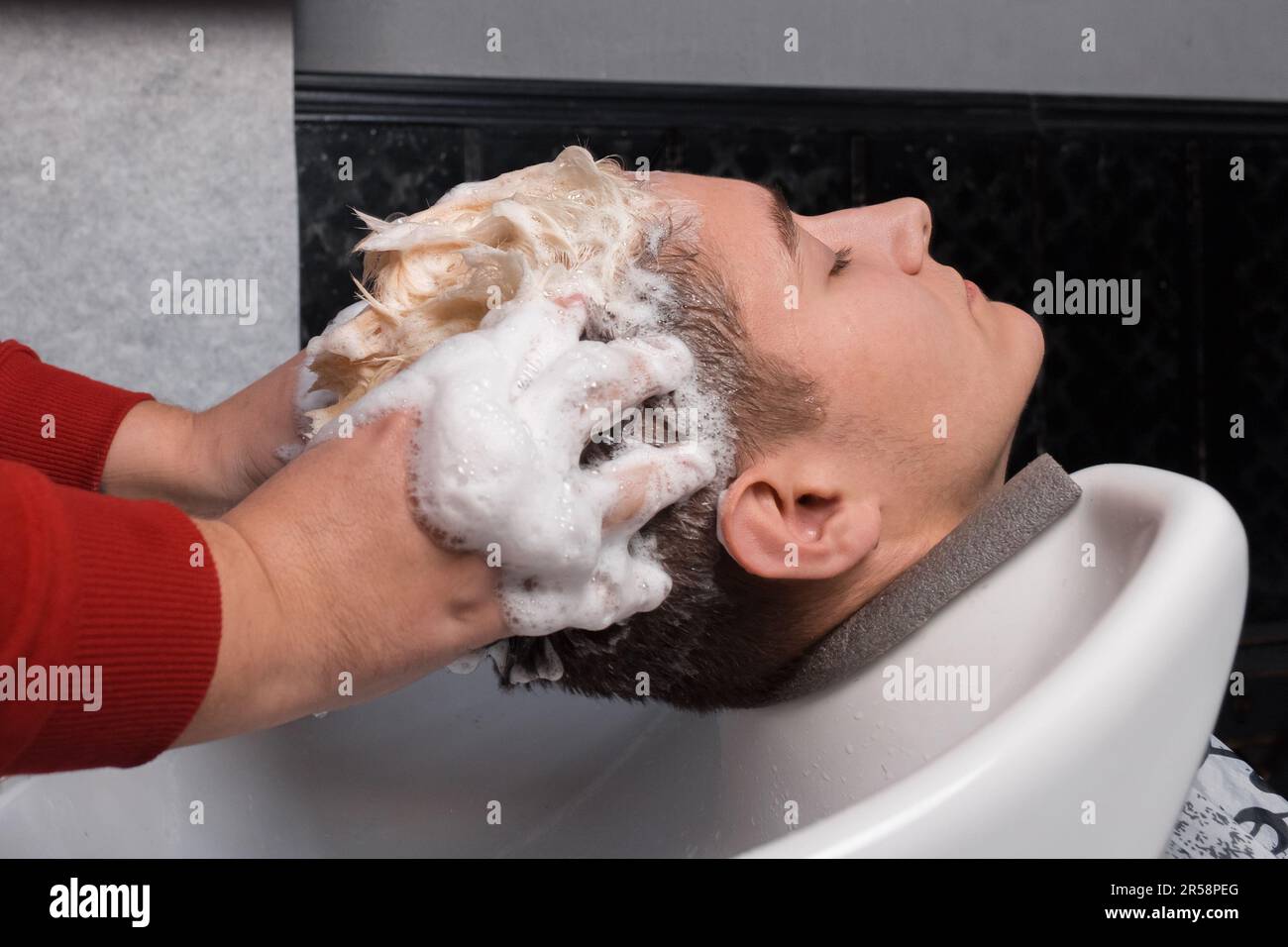 Les mains du coiffeur laver les cheveux et la tête du client du coiffeur avec de la mousse dans l'évier avant de couper les cheveux. Banque D'Images