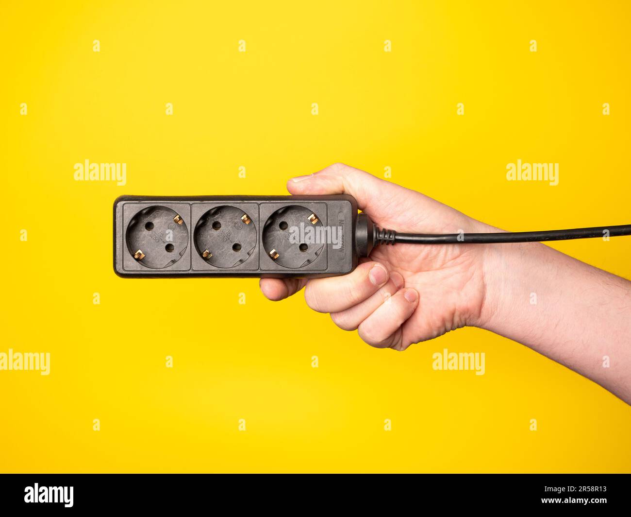 Une main tient une multiprise. Pas de face, fond jaune. Banque D'Images