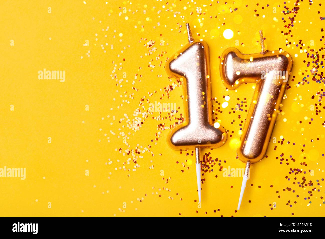 Bougies d'or sous la forme du numéro dix-sept sur fond jaune avec confetti. célébration de 17 ans. Banque D'Images