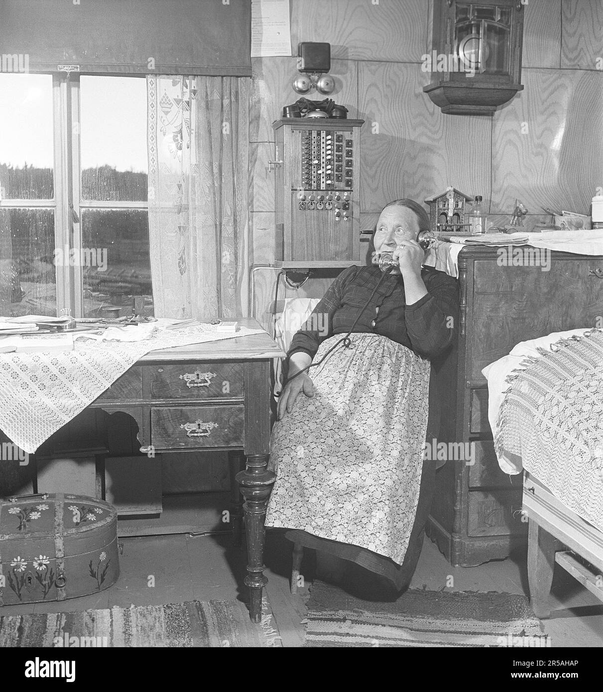Une femme âgée dans la zone peu peuplée de Norrbotten à la maison, près du tableau de commutation téléphonique fixé au mur. Il était courant dans les villages des zones peu peuplées que quelqu'un avait le standard téléphonique à la maison et était responsable de la connexion des appels téléphoniques de et vers les résidents du village. Vous pouvez également y aller et appeler si vous n'avez pas de téléphone. Suède 1949. Kristoffersson réf. AS75-4 Banque D'Images