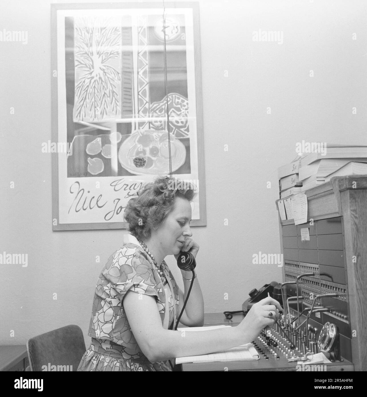 Téléphonie dans le 1950s. Une femme travaillant à un standard téléphonique comme opérateur. Un système de communication téléphonique qui a été actionné manuellement où les appels entrants ont été renvoyés et redirigés vers un autre numéro de téléphone par l'opérateur, dans ce cas localement dans le bâtiment desservant une entreprise, un hôtel ou une organisation avec de nombreuses lignes téléphoniques internes. L'opérateur du standard peut prendre des messages et vous mettre en attente si la ligne était occupée. Suède 1958. Banque D'Images