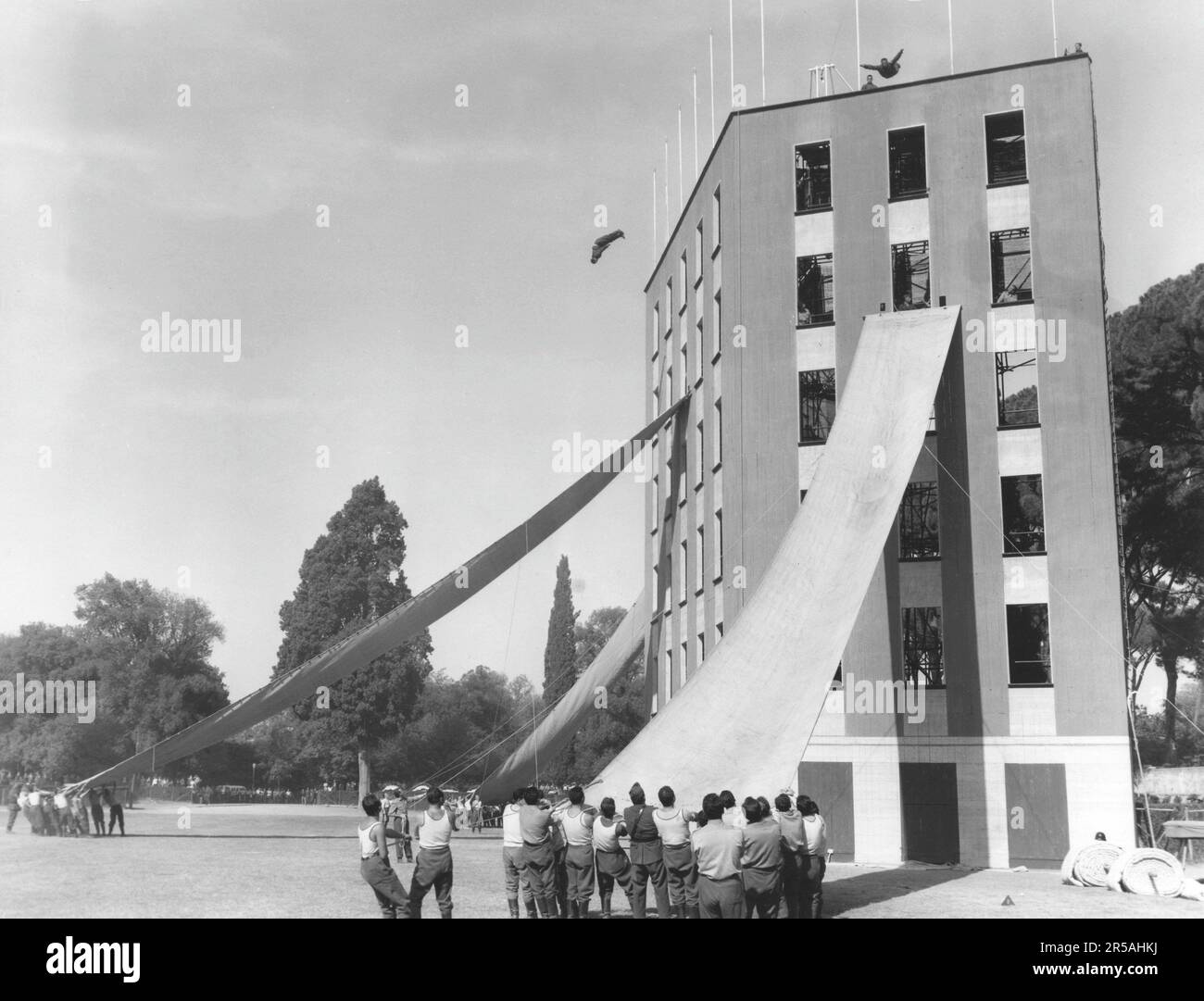 Dans le 1950s. Exercice effectué dans un lieu de formation pour les pompiers et les sauveteurs. De longs morceaux de tissu sont attachés à la façade des bâtiments et étirés par les pompiers, de sorte qu'il devient semblable à un toboggan, faisant le saut de l'immeuble à lui, un sauvetage plus sûr et plus lent. 1956 Banque D'Images