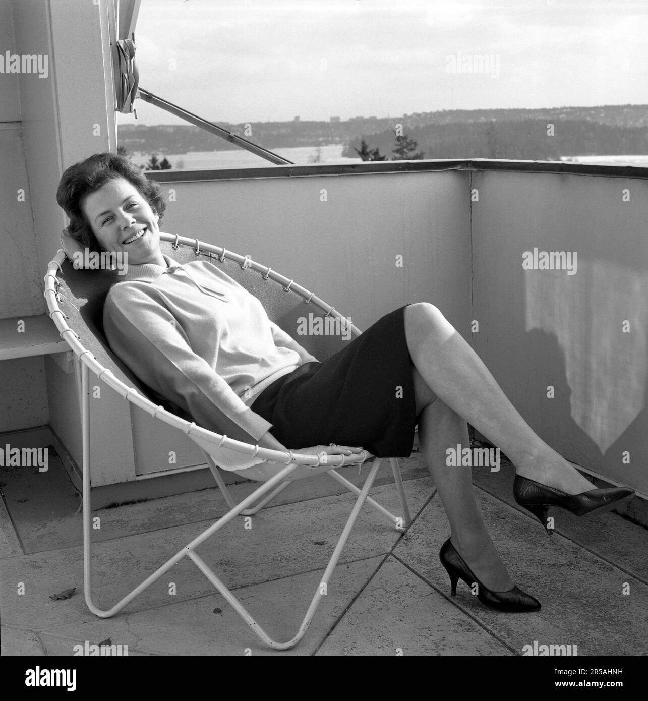 Décoration de la maison du 1960s. Une femme est assise confortablement dans la chaise de pont de 1950s 1960s conçu avec des tuyaux en acier avec un centre rond et quatre jambes. Le siège est en cuir. Un design populaire à l'époque avec de nombreuses variétés différentes, certaines plus connues que d'autres. Elle est actrice Sickan Carlsson 1915-2011 dans à la maison sur le balcon. Suède 1964 Banque D'Images