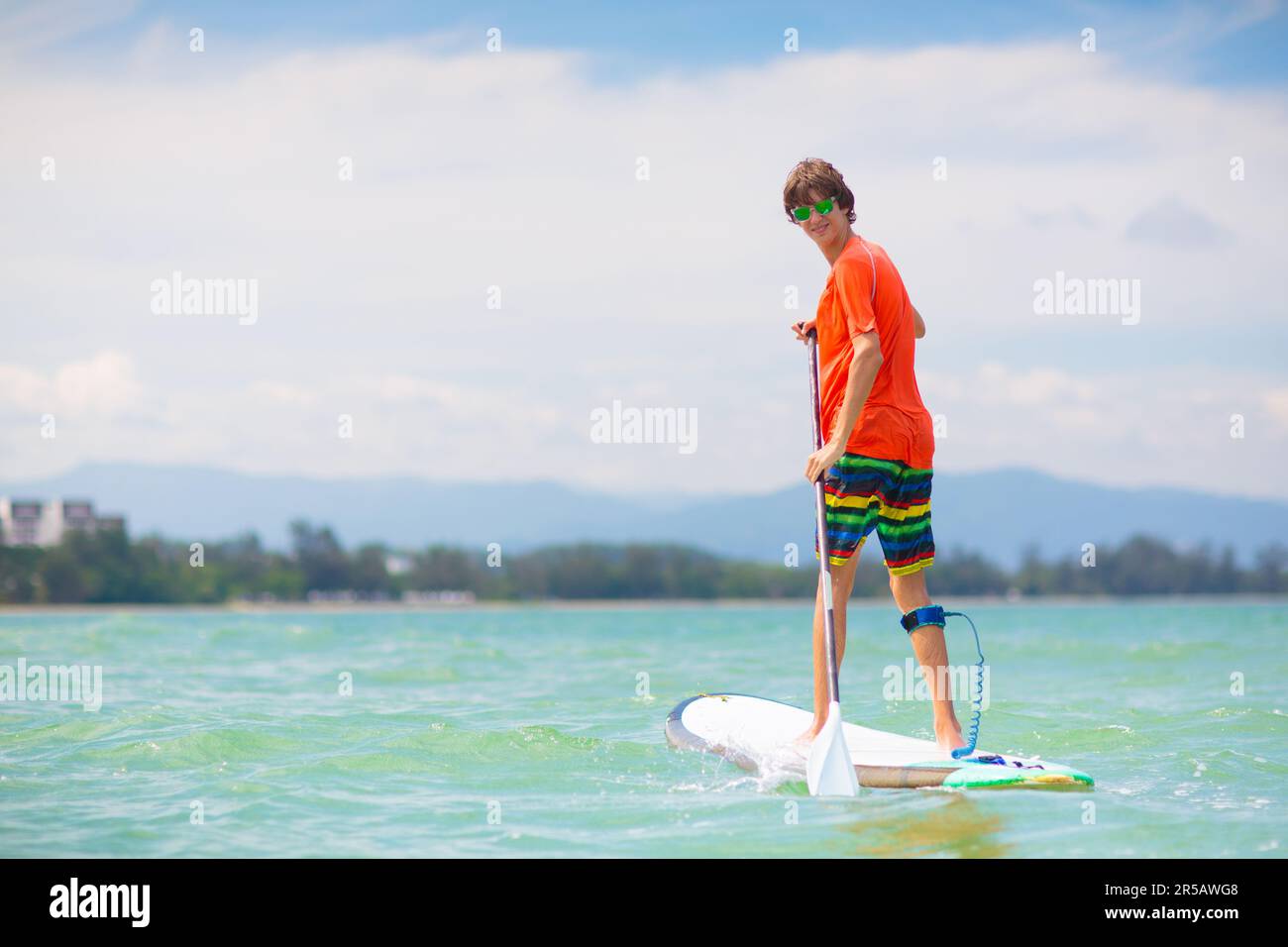 Jeune homme sur le paddle-board debout. Jeux aquatiques et sports de plage. Sports de plein air sains pour les vacances d'été sur l'île tropicale. Activité vacances. Banque D'Images