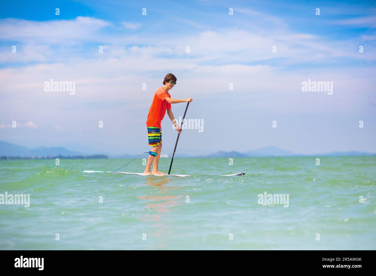 Jeune homme sur le paddle-board debout. Jeux aquatiques et sports de plage. Sports de plein air sains pour les vacances d'été sur l'île tropicale. Activité vacances. Banque D'Images