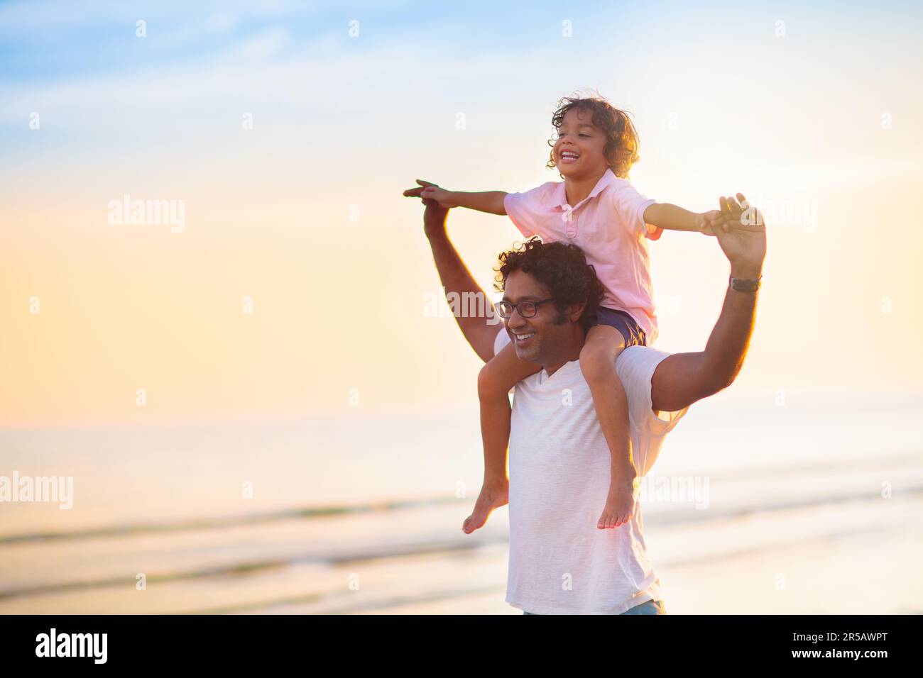 Père et enfant jouant sur la plage tropicale au coucher du soleil. Vacances d'été en famille à la station balnéaire. Papa jouant avec les enfants le soir ensoleillé au bord de l'océan. Banque D'Images