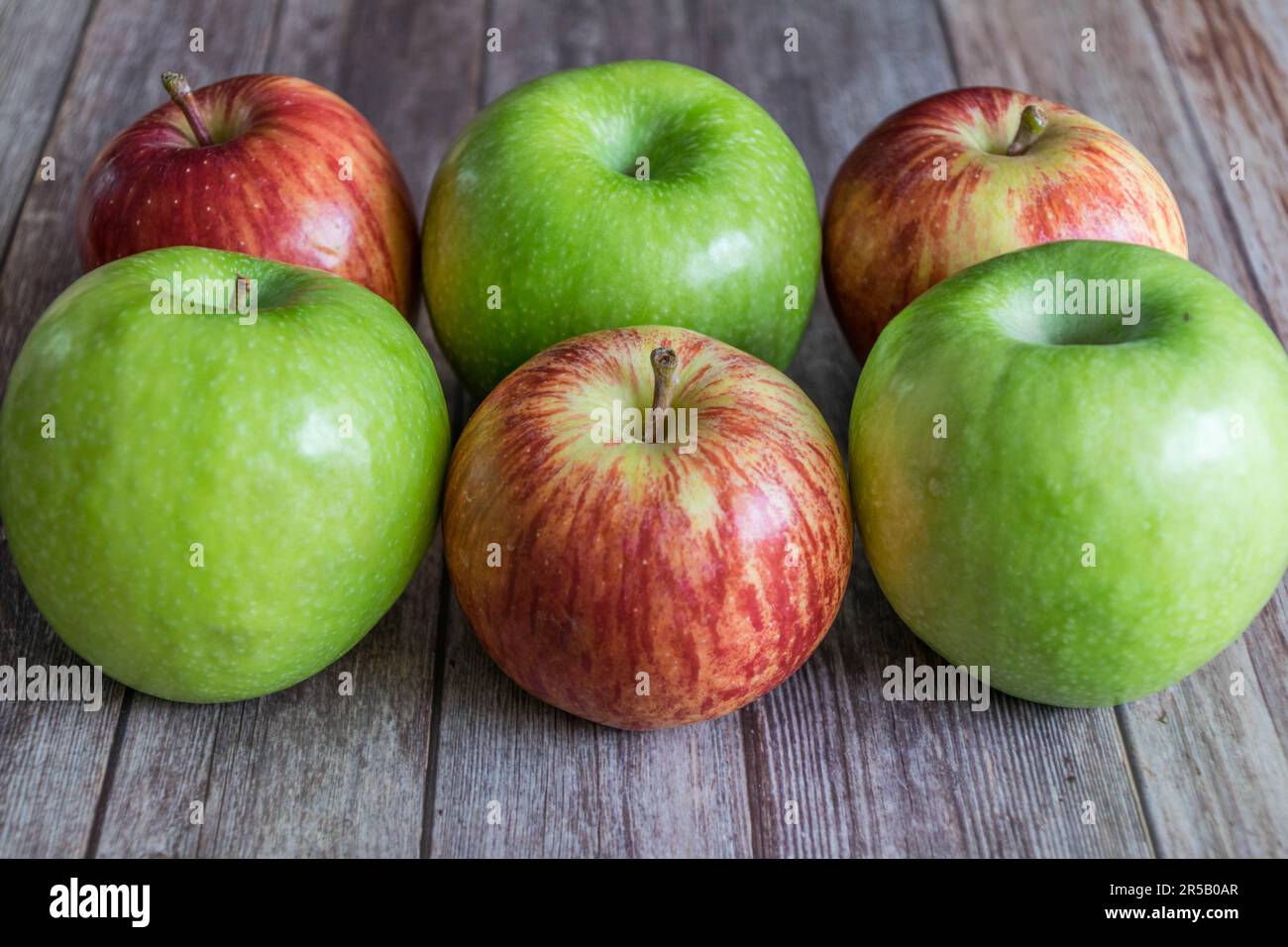 Quatre pommes mûres en rangée sur une surface de table en bois, prêtes à la consommation Banque D'Images
