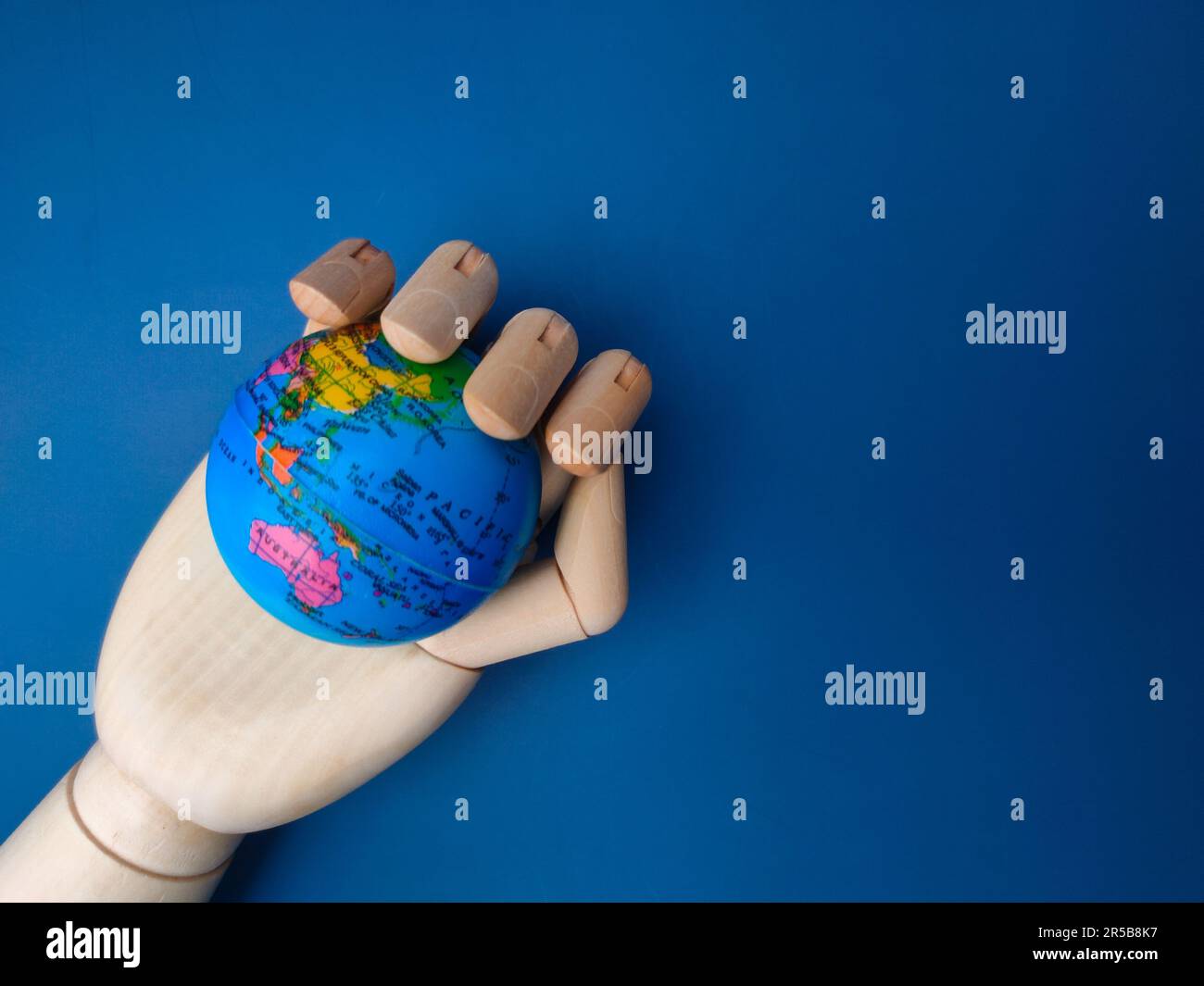 Une main en bois s'étend vers l'extérieur, avec un petit globe bleu dans sa paume Banque D'Images