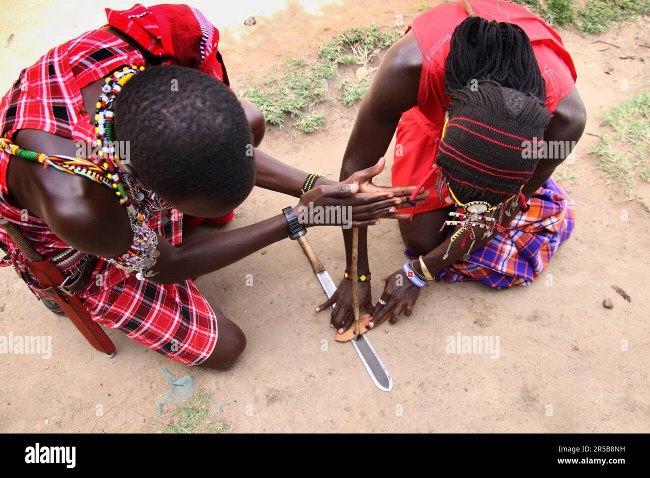 Les membres de la tribu Maasai Mara font feu en utilisant une herbe sèche bâton et un couteau traditionnel de 406mm buffle plat masai Mara pour démontrer une méthode de départ de feu Banque D'Images