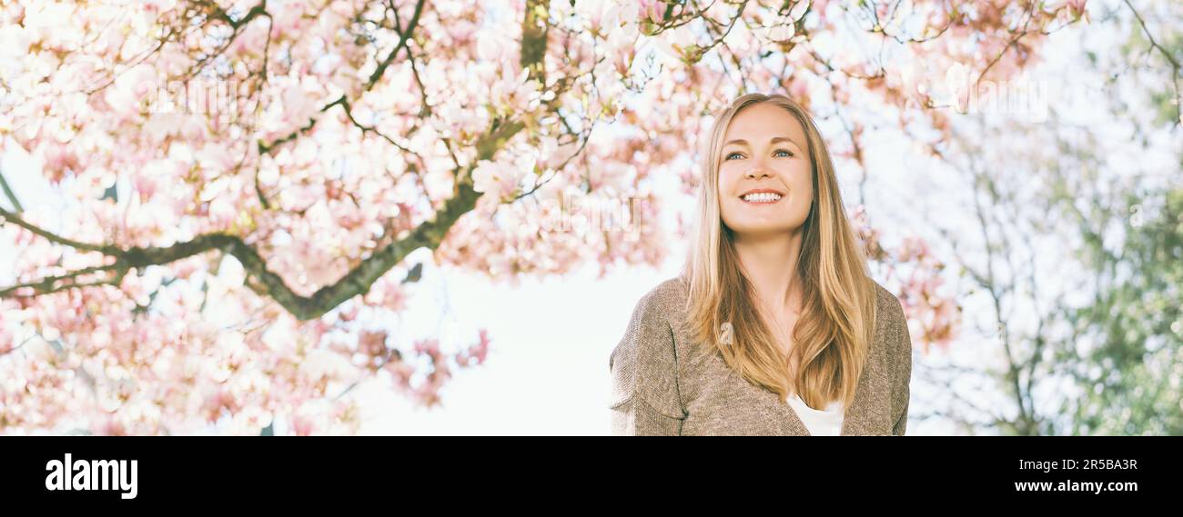 Arrière-plan de bannière panoramique avec jeune belle femme heureuse avec des cheveux blonds, posant sous le magnolia en fleur Banque D'Images