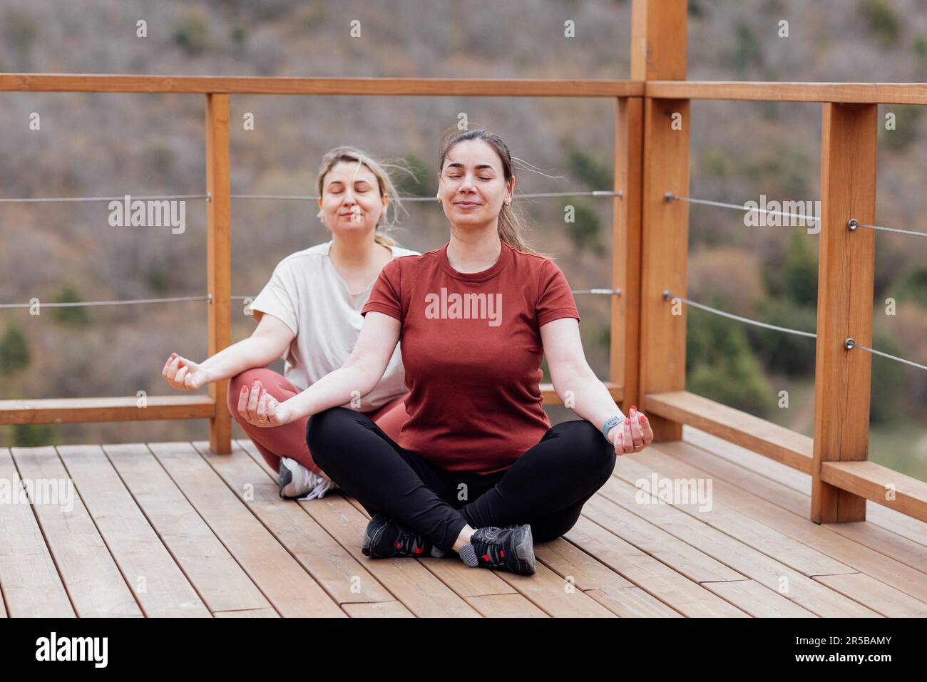 Deux jeunes femmes s'entraîner à l'asana yoga dans le parc. Les filles souriantes sont assises en position lotus. Les amies méditent sur une plate-forme en bois à ciel ouvert. En bonne santé Banque D'Images