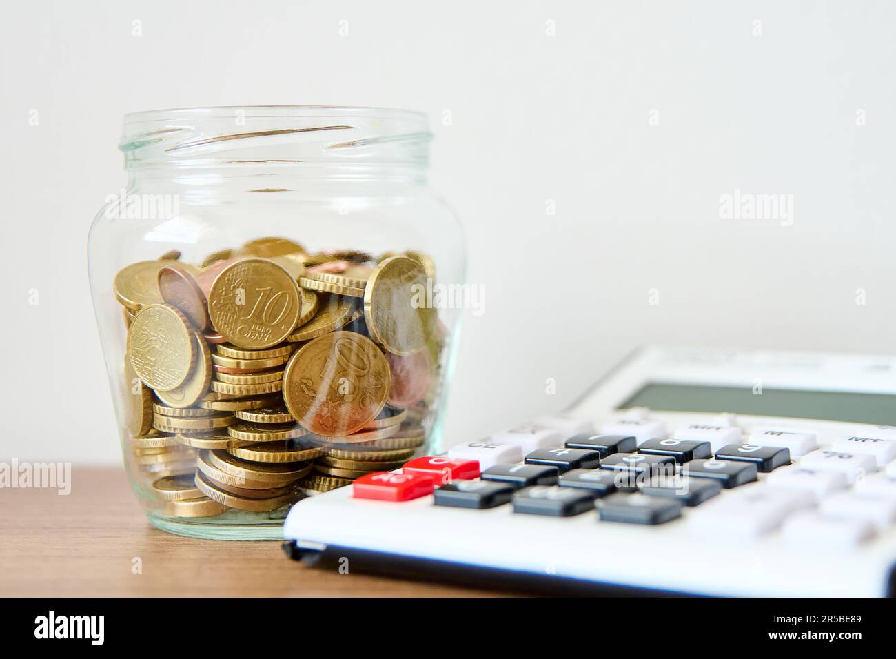 Une table en bois avec un pot en verre contenant des pièces de monnaie et une calculatrice située sur le dessus Banque D'Images