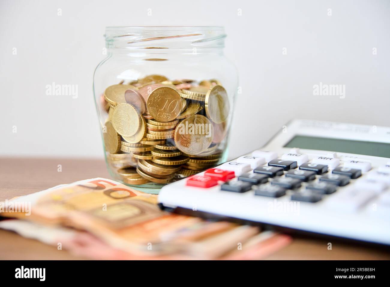 Une table en bois avec un pot en verre contenant des pièces de monnaie et une calculatrice située sur le dessus Banque D'Images