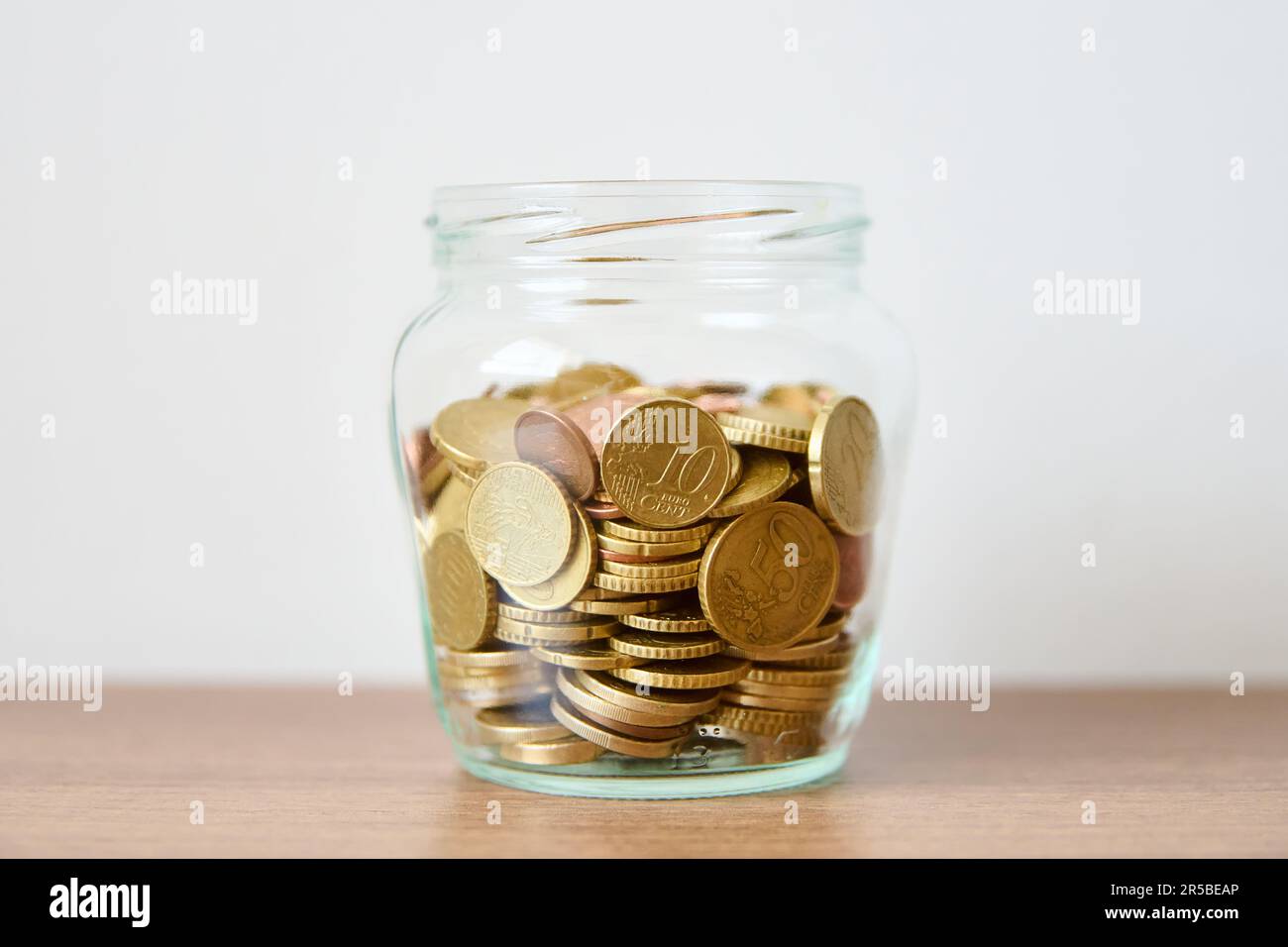 Pièces de monnaie dans un pot en verre sur la table avec fond blanc Banque D'Images