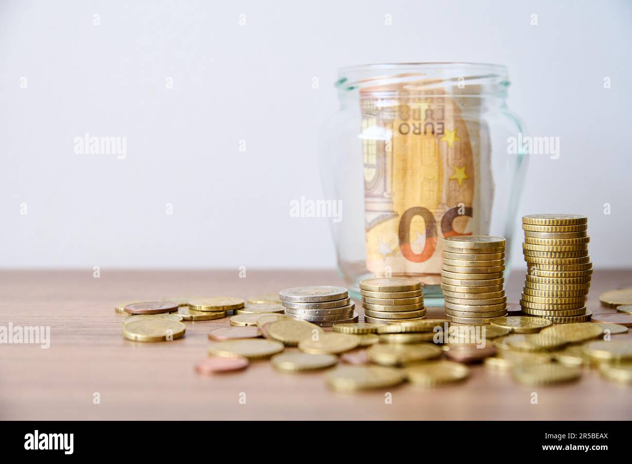 Pièces de monnaie dans un pot en verre sur la table avec fond blanc Banque D'Images