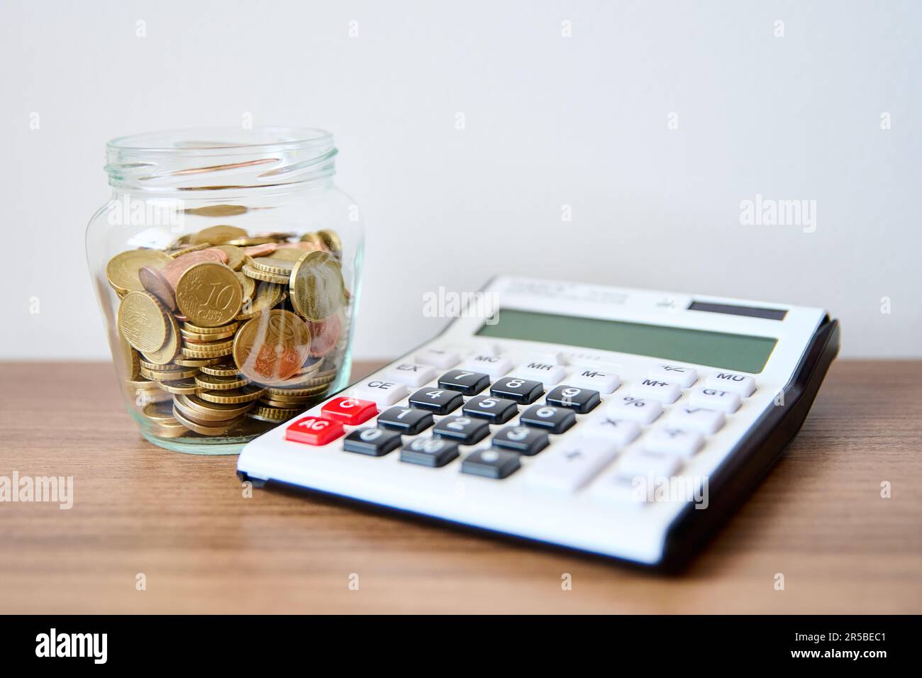 Une table en bois avec un pot en verre contenant des pièces de monnaie et une calculatrice située sur le dessus Banque D'Images