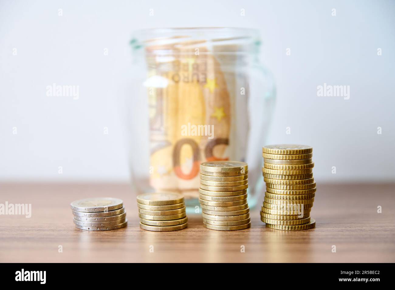 Pièces de monnaie dans un pot en verre sur la table avec fond blanc Banque D'Images