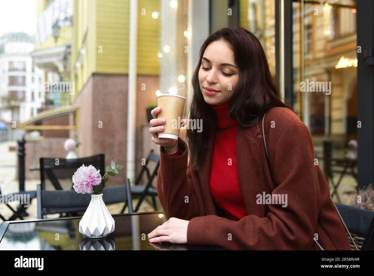 Belle femme souriant avec une tasse de café dehors, buvant du café sur la terrasse dans un café. Banque D'Images
