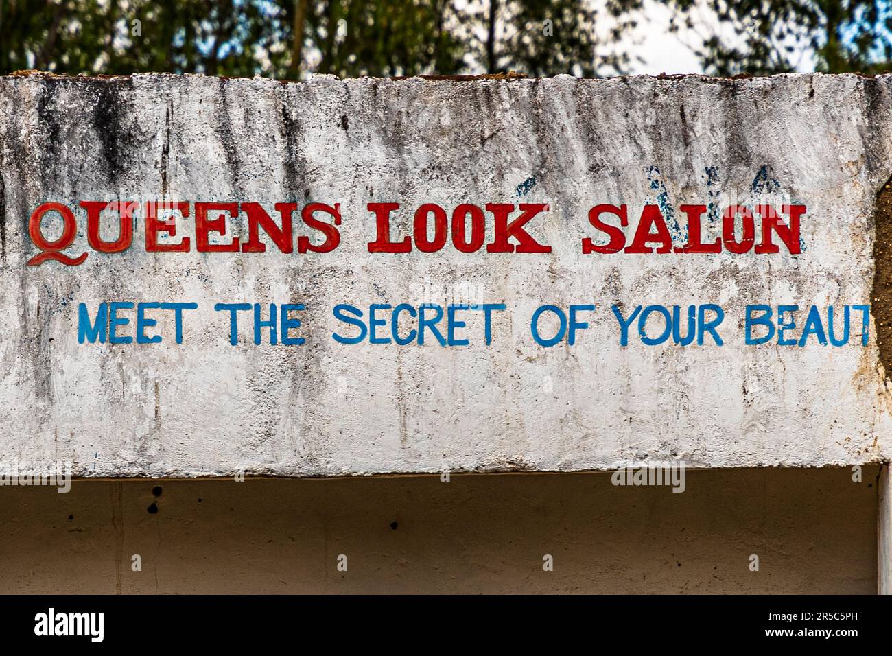 Slogan publicitaire d’un salon de coiffure peint sur un mur à Chitimbe, Malawi : "Queens Look Salon – Découvrez le secret de votre beauté." Banque D'Images